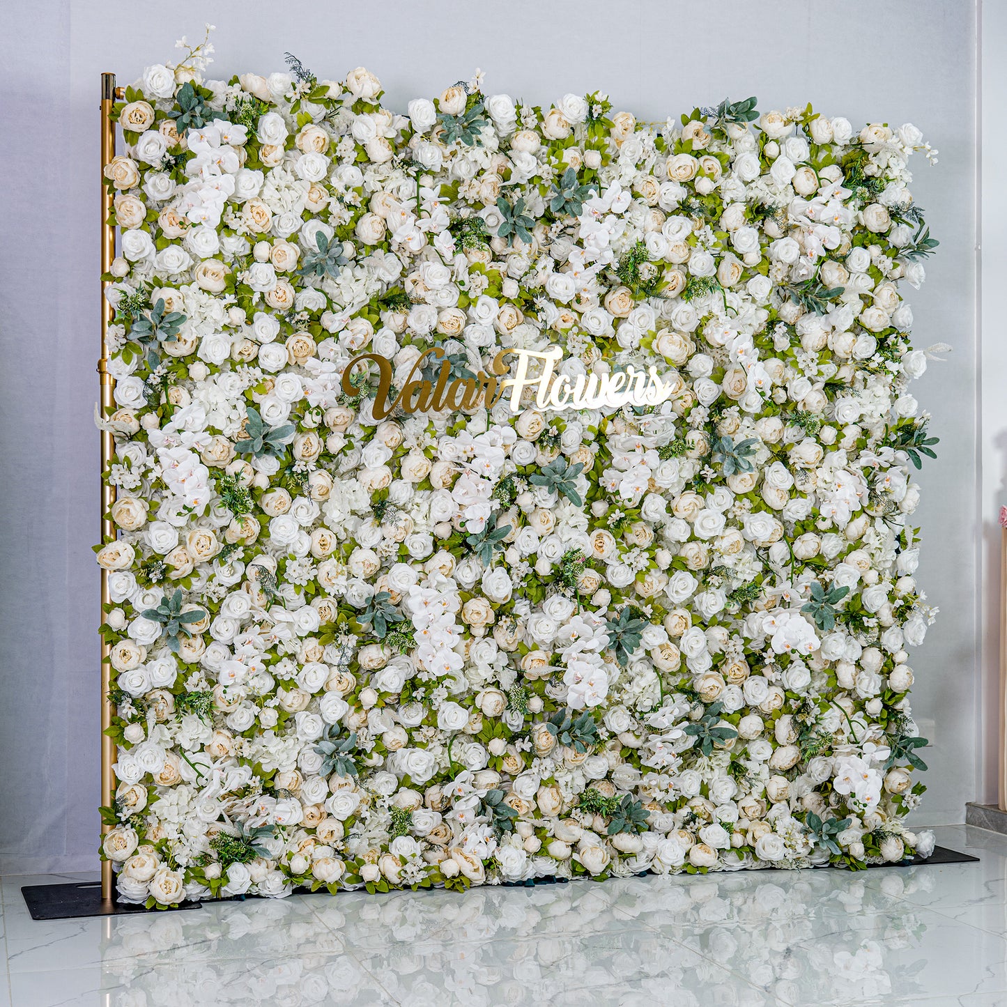 This backdrop is a lush, elegant display of white artificial flowers interspersed with green foliage. Densely packed, it creates a soft, romantic atmosphere. The golden “Valar Flowers” sign adds a touch of sophistication, ideal for weddings or upscale events. 