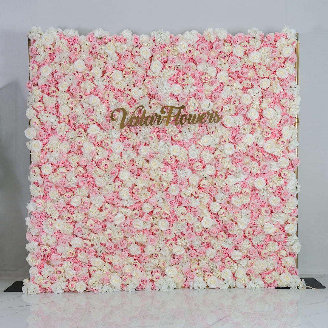 This photo showcases a lush floral backdrop. It is densely covered with a blend of pink and white roses, creating a soft and romantic color scheme. The backdrop also features the text "Valar Flowers" in elegant gold lettering. Ideal for weddings, engagement parties, or bridal showers, it exudes a dreamy and elegant style, perfect for adding a touch of romance to any event.