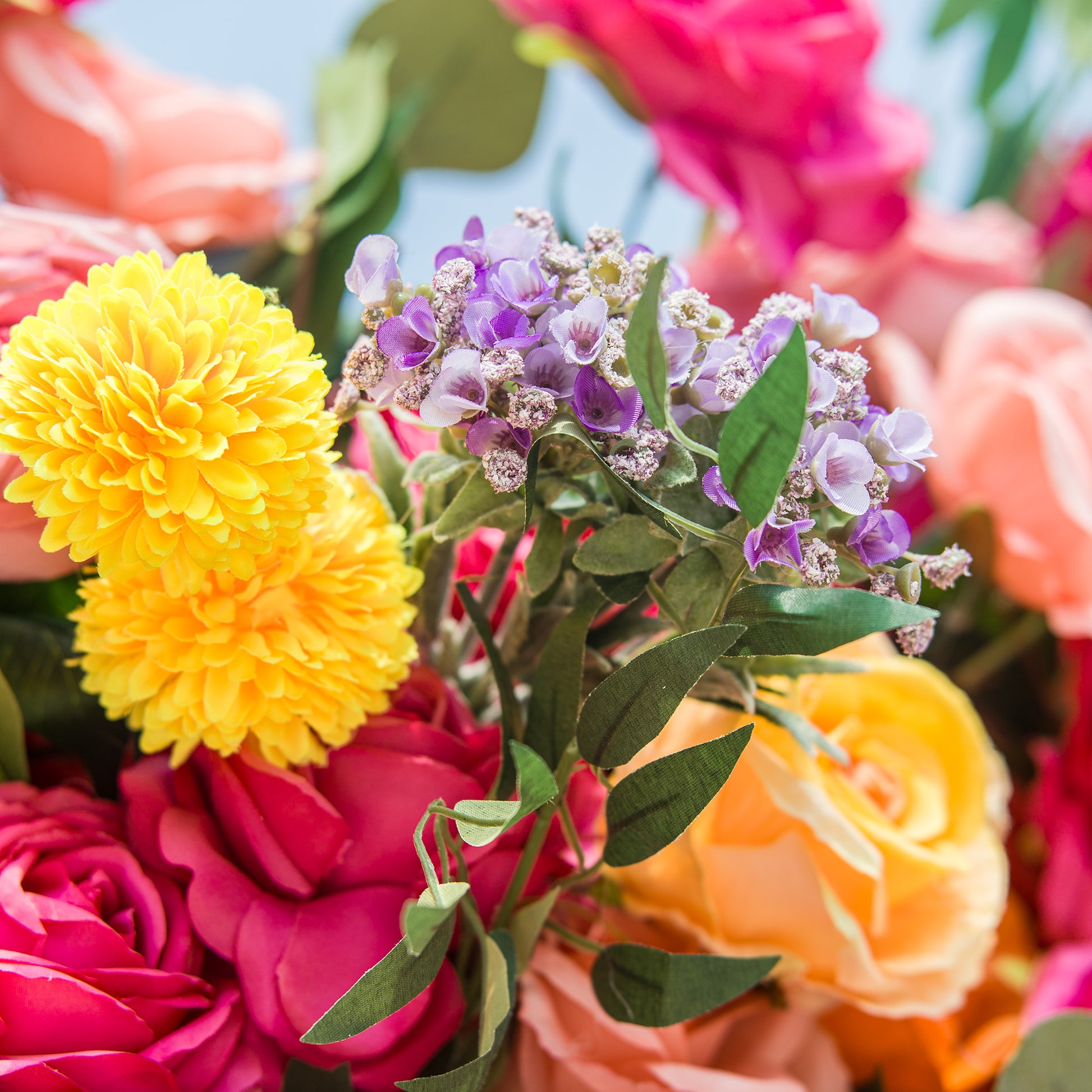A close - up of a vibrant floral arrangement! Bright yellow pom - pom - like flowers, delicate purple blossoms with tiny white centers, and lush green leaves stand out. Surrounding them are rich pink roses and soft peach - colored blooms. The varied textures and vivid hues create a lively, eye - catching display, perfect for adding a burst of color to any setting. 