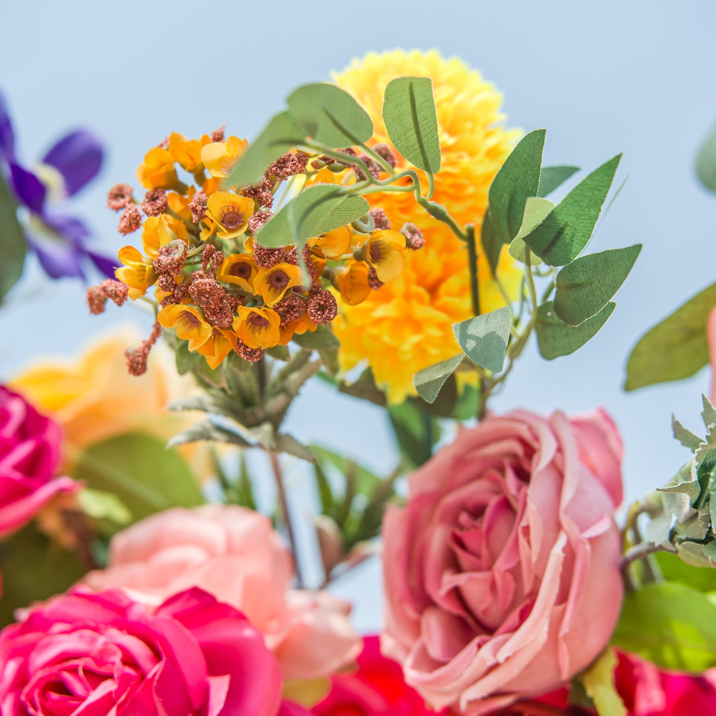 A vibrant close - up of a floral arrangement! Bright yellow flowers, including a fluffy bloom and a clustered, textured variety, stand out. Surrounding them are soft pink and deep pink roses, with hints of purple blossoms and green foliage. The clear blue sky backdrop enhances the vivid colors, creating a lively, eye - catching display full of natural beauty and charm. 