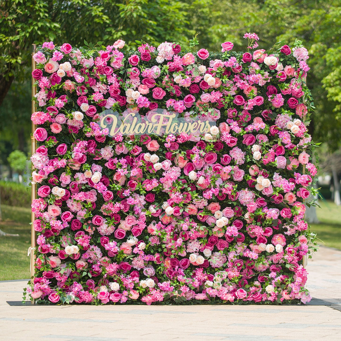 This photo showcases a large, square floral backdrop densely covered with an array of pink and white roses, along with other assorted pink flowers, all set against lush green foliage. The text “ValarFlowers” in elegant lettering stands out prominently. Ideal for events like a “Pink Paradise” garden party or a vibrant wedding, it exudes a lively and romantic charm, perfect for outdoor celebrations. 