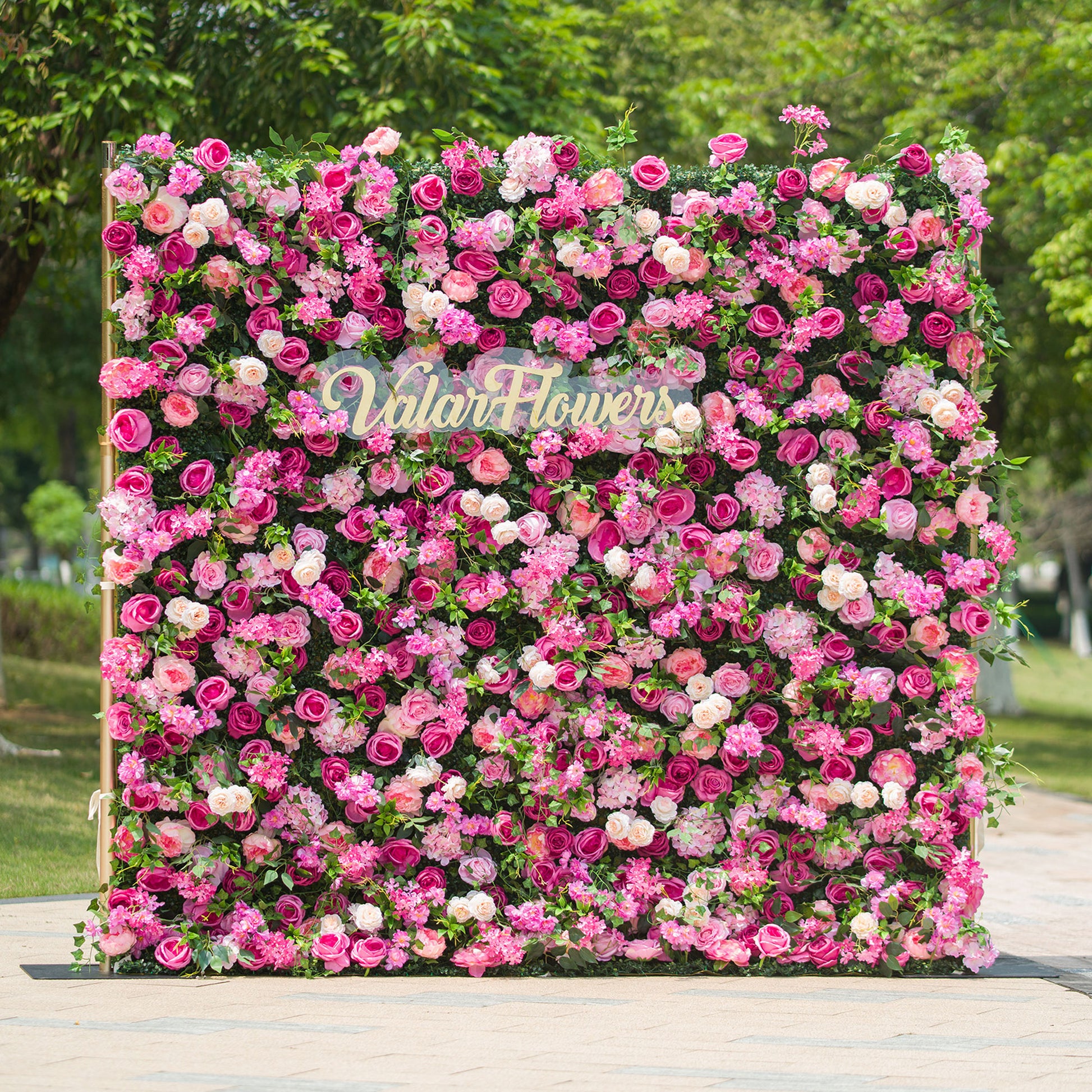 This photo showcases a large, square floral backdrop densely covered with an array of pink and white roses, along with other assorted pink flowers, all set against lush green foliage. The text “ValarFlowers” in elegant lettering stands out prominently. Ideal for events like a “Pink Paradise” garden party or a vibrant wedding, it exudes a lively and romantic charm, perfect for outdoor celebrations. 