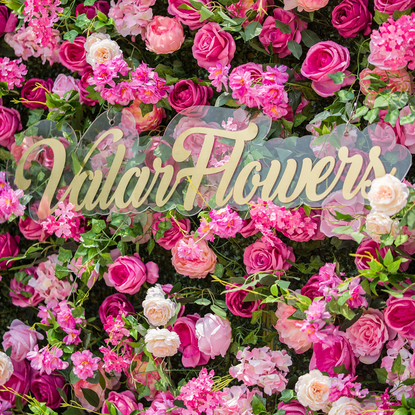 This photo showcases a dense floral backdrop brimming with an array of pink and white roses, along with other assorted pink flowers, all nestled among lush green foliage. The text “ValarFlowers” in elegant golden lettering stands out prominently. The vibrant blooms create a lively, romantic atmosphere, ideal for events like garden weddings or spring - themed parties. 