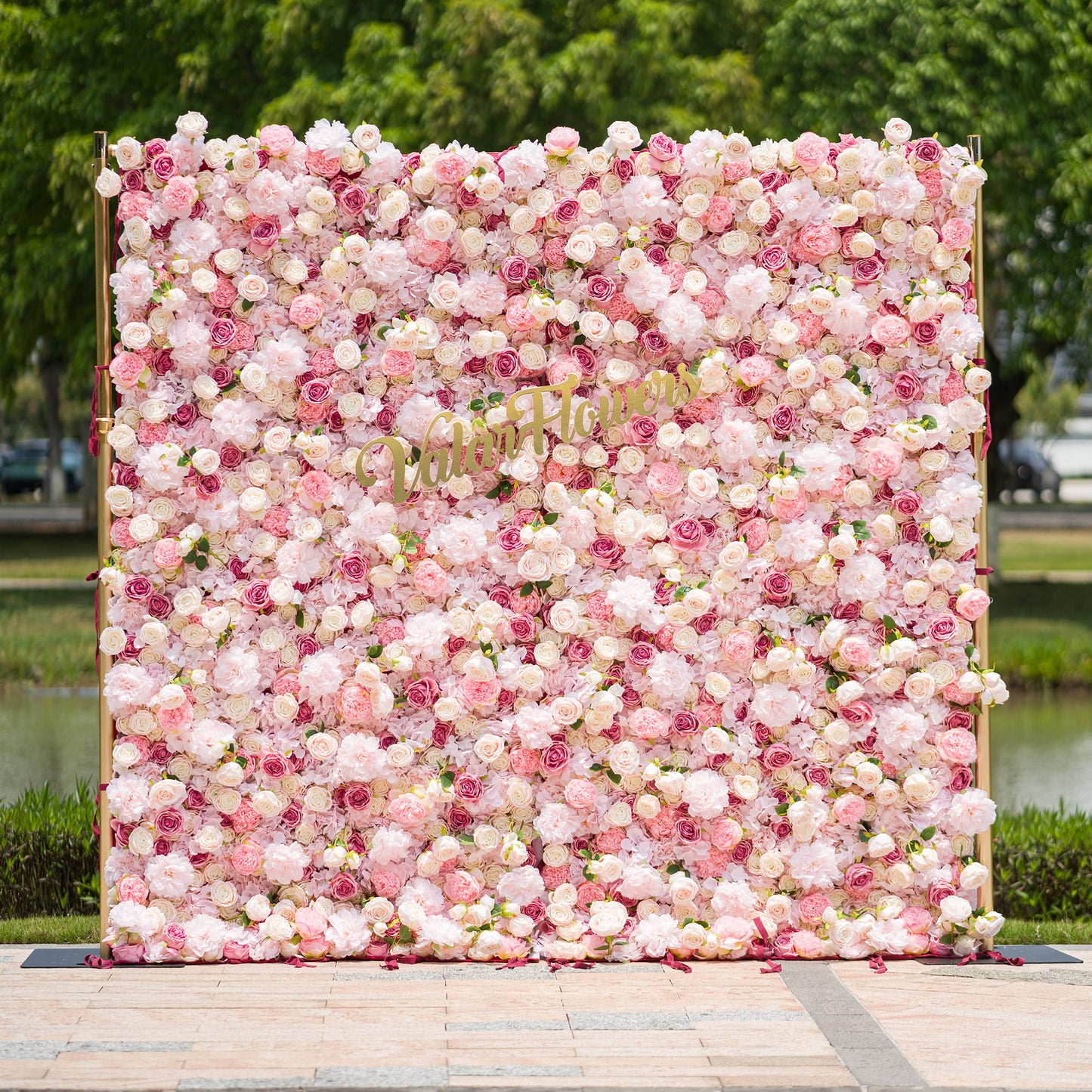 This photo from ValarFlowers showcases a large, lush floral backdrop. It is densely filled with an array of pink and white roses and peonies, creating a soft and romantic atmosphere. The backdrop is framed by golden poles, adding a touch of elegance. Ideal for weddings, bridal showers, or a “Blossoming Love” - themed event, it serves as a beautiful decorative element, exuding charm and grace. 