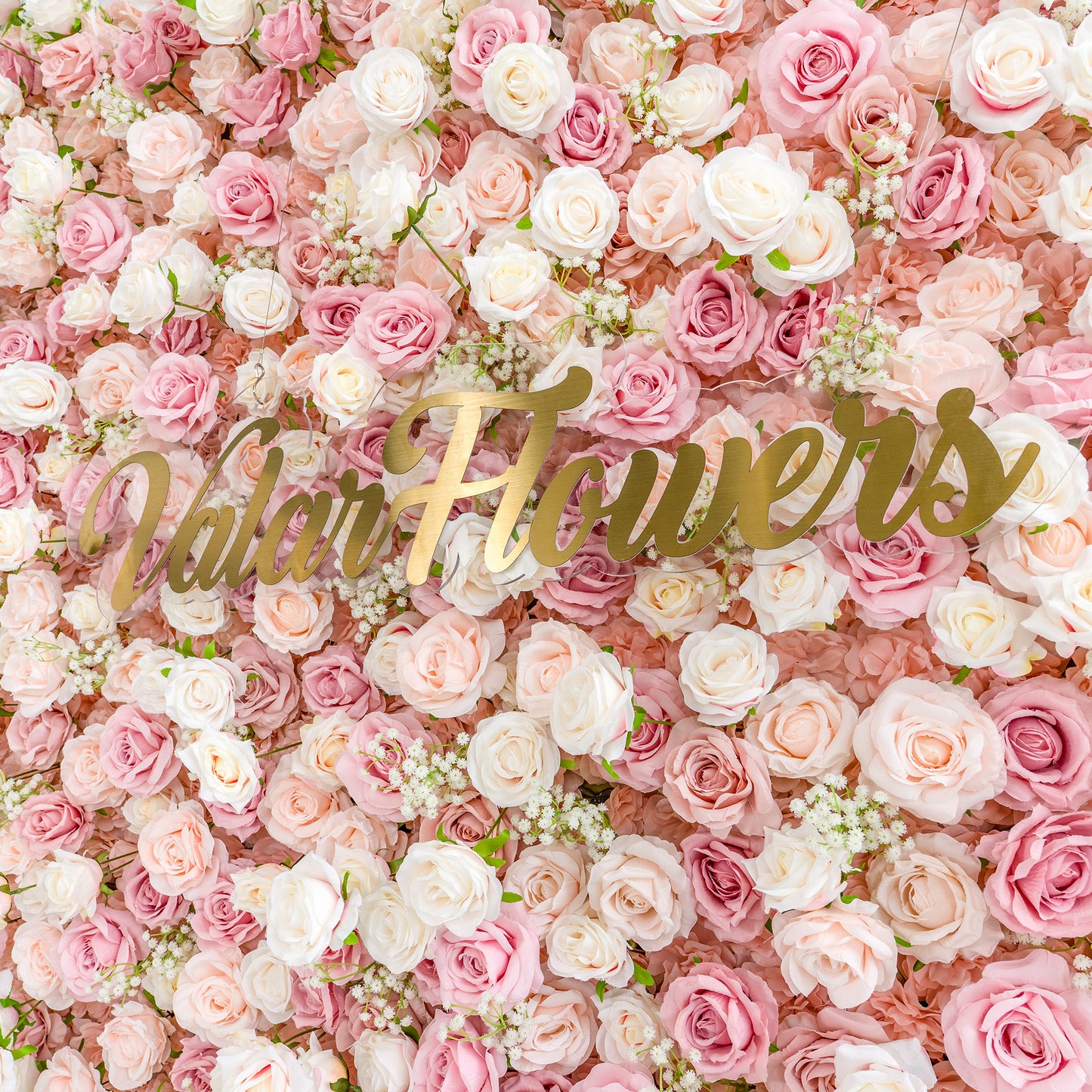 This photo showcases a lush floral backdrop densely packed with pink and white roses, interspersed with delicate baby's breath. The soft pastel color palette creates a romantic and dreamy atmosphere. The words "Valar Flowers" in elegant gold lettering stand out prominently. Ideal for weddings, bridal showers, or other romantic events, it exudes a refined and tender style. 