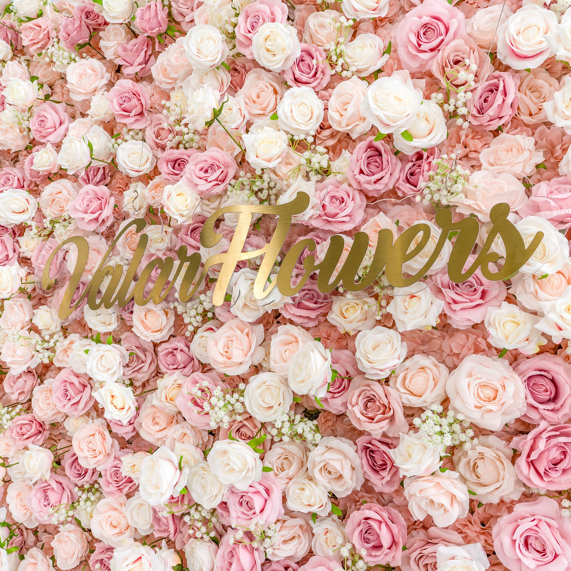 This photo showcases a lush floral backdrop densely packed with pink and white roses, interspersed with delicate baby's breath. The soft pastel color palette creates a romantic and dreamy atmosphere. The words "Valar Flowers" in elegant gold lettering stand out prominently. Ideal for weddings, bridal showers, or other romantic events, it exudes a refined and tender style. 