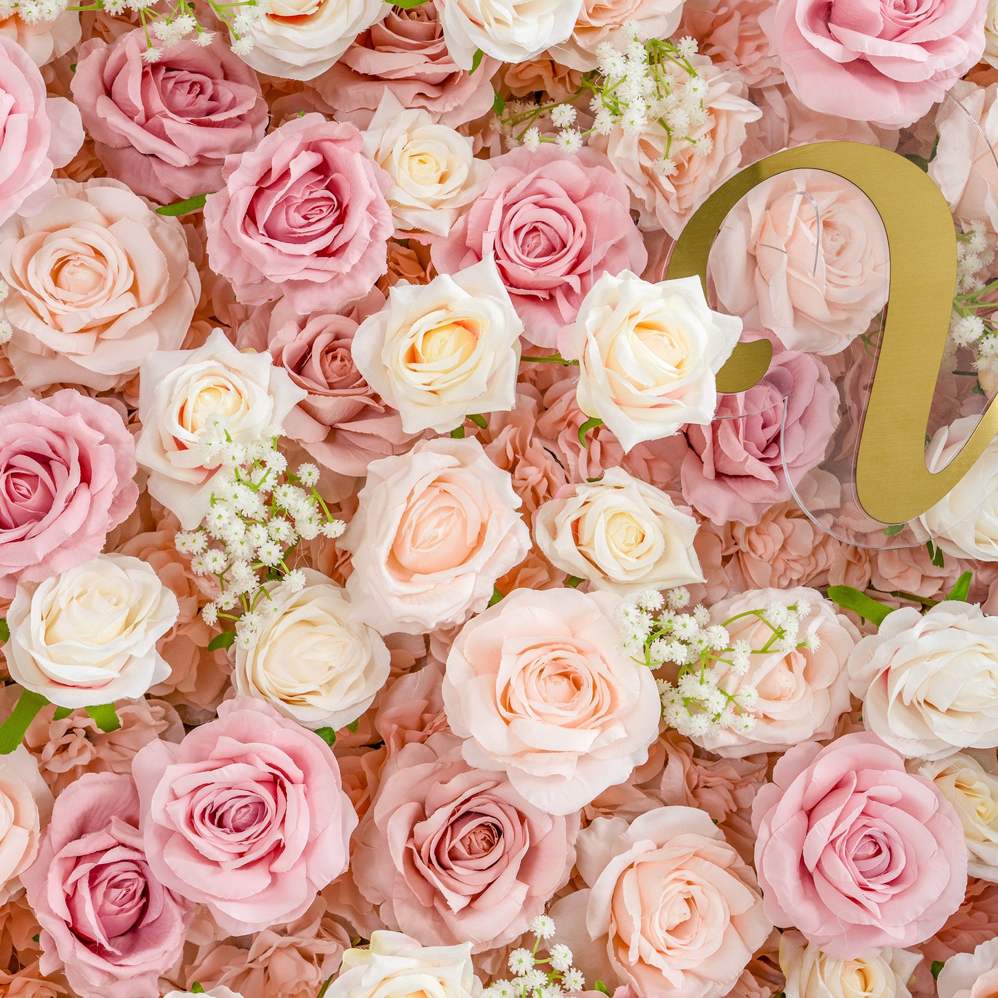 This photo showcases a lush arrangement of roses in soft shades of pink, peach, and white, interspersed with delicate baby's breath. The dense floral display creates a dreamy and romantic ambiance. Ideal for weddings, bridal showers, or other romantic events, it exudes elegance and tenderness. The partially visible golden letter adds a touch of sophistication. 