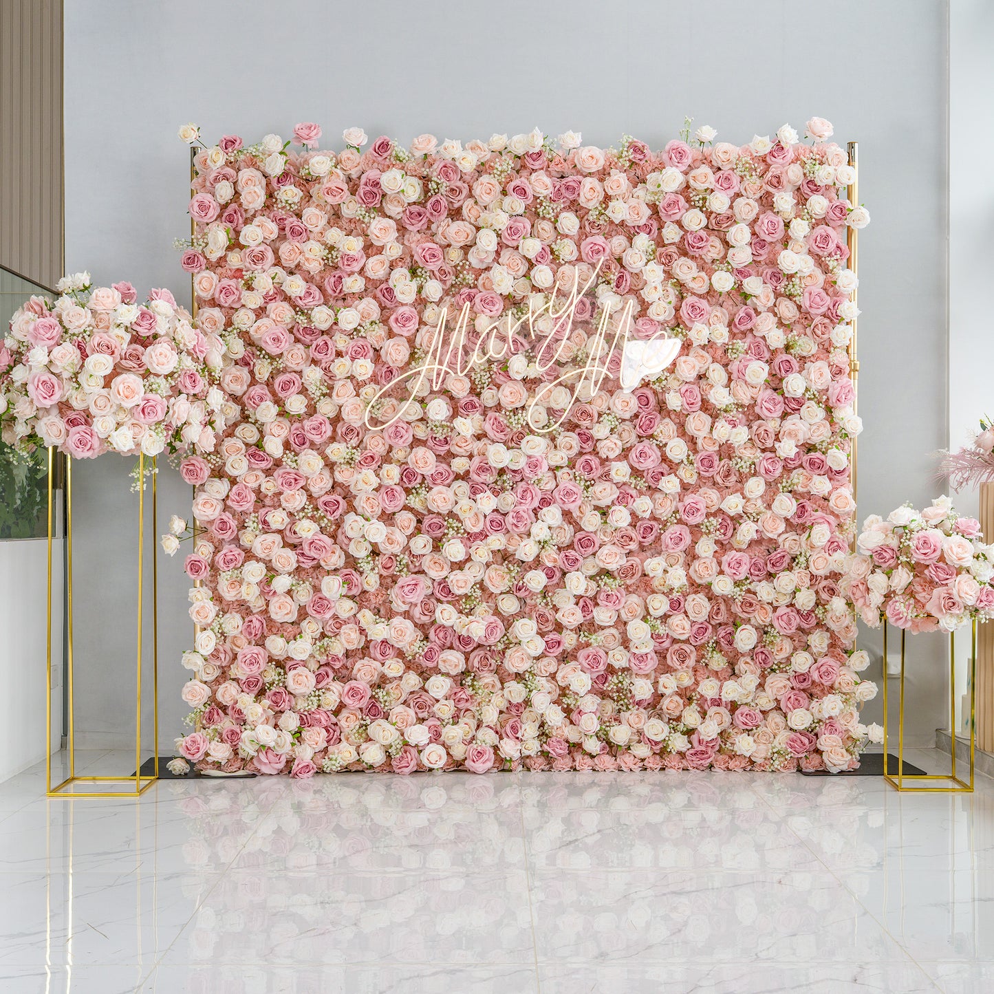 This photo presents a large floral backdrop densely covered with pink and white roses, creating a soft, romantic atmosphere. The cursive text "Mary Me" with a heart symbol adds a personalized touch. Flanking the backdrop are two golden - framed floral arrangements on stands, matching the backdrop's color scheme.