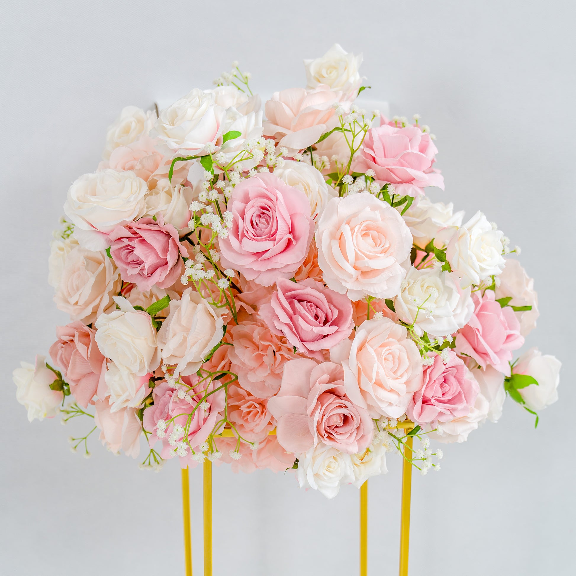 This photo showcases a lush, elegant floral arrangement. A dense cluster of pink and white roses, interspersed with delicate baby's breath, forms a rounded bouquet. The flowers are mounted on a golden stand, which provides a striking contrast to the soft pastel hues of the blooms. Set against a plain, light - colored background, the arrangement exudes a romantic and refined charm, perfect for events like weddings or upscale celebrations. 