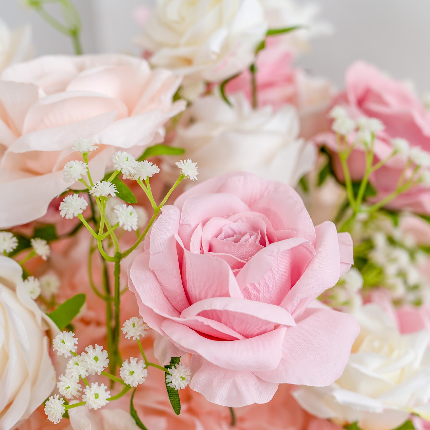 This photo captures a close - up view of a delicate floral arrangement. At the forefront is a soft pink rose with its petals elegantly layered, surrounded by a mix of white roses and tiny white baby's breath flowers. The green stems and leaves add a touch of freshness, creating a charming and romantic scene. The pastel color palette exudes a gentle, soothing aesthetic, perfect for evoking feelings of tenderness and beauty. 