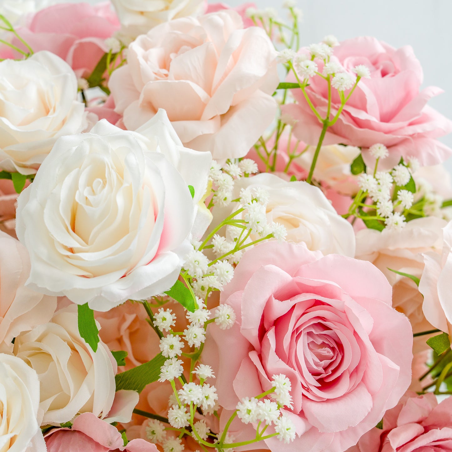 This photo showcases a lush arrangement of roses in soft pastel shades of pink and white, interspersed with delicate baby's breath flowers. The petals of the roses are intricately layered, creating a full and textured appearance. The green stems and leaves add a touch of natural freshness. The overall composition exudes a romantic and elegant ambiance, perfect for occasions like weddings or celebrations. 