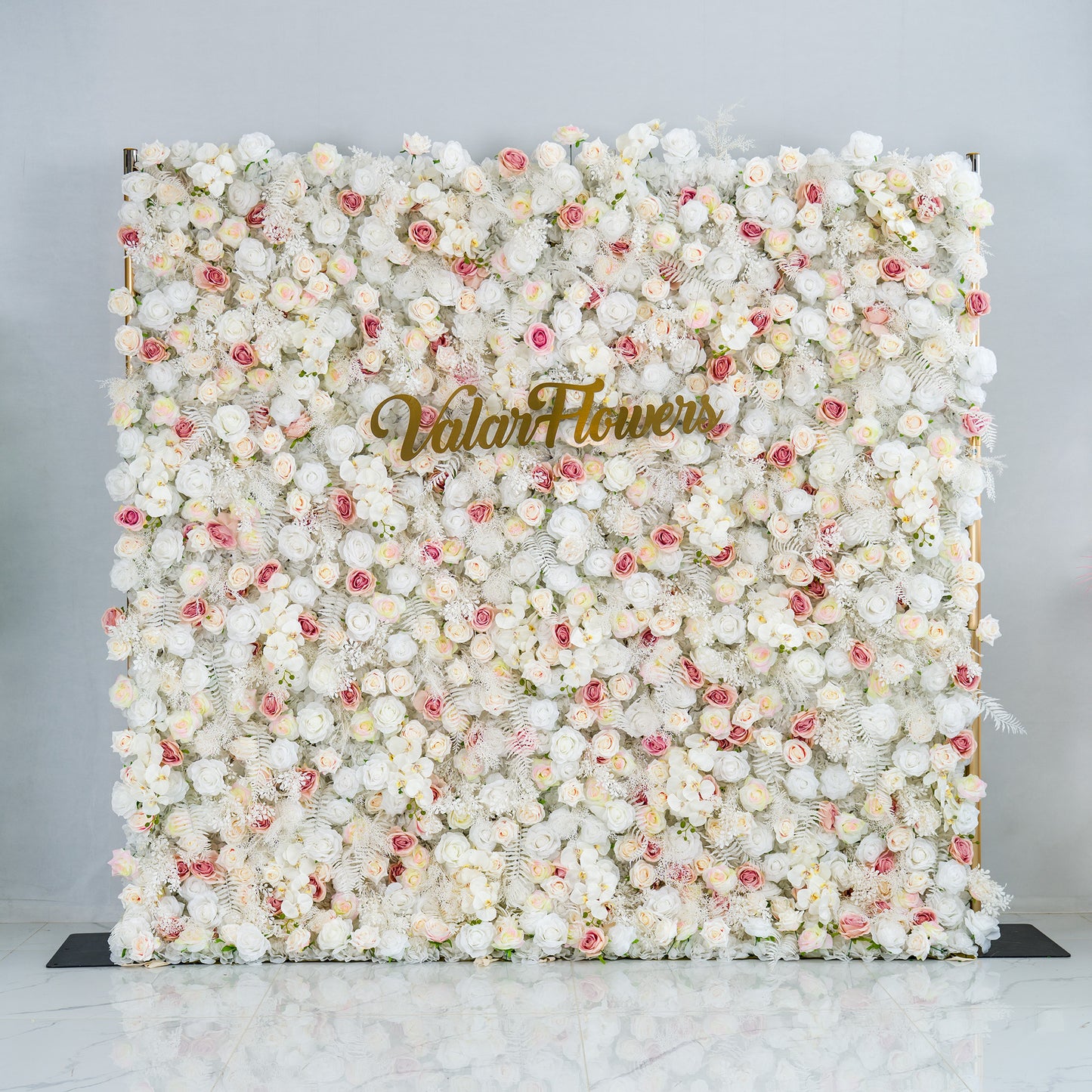 This photo showcases a lush floral backdrop densely covered with white roses and interspersed with delicate pink roses. The soft, neutral color palette creates an elegant and serene atmosphere. The words "Valar Flowers" in elegant gold lettering stand out prominently. Ideal for weddings, upscale galas, or sophisticated events, it exudes a refined and dreamy style. 