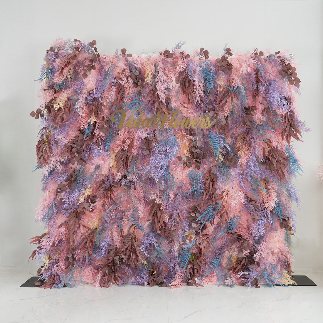 This backdrop is a lush, colorful foliage arrangement. It features a blend of pink, purple, and brown leaves, with some blue fern - like fronds adding contrast. The elegant "Valar Flowers" sign in gold lettering stands out amidst the greenery. Ideal for weddings, parties, or upscale events, it exudes a romantic and sophisticated style.