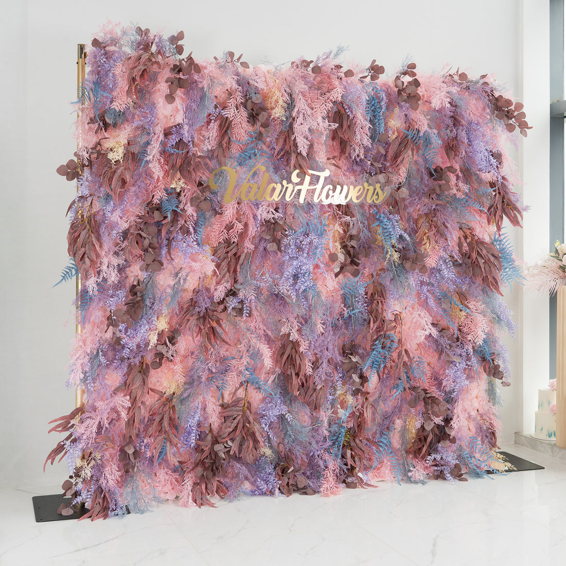 This backdrop is a vibrant and lush foliage display. It combines a dreamy palette of pinks, purples, and blues, interspersed with earthy brown leaves. The elegant gold text &quot;Valar Flowers&quot; is prominently featured. Ideal for weddings, galas, or upscale parties, it exudes a romantic and whimsical style, creating a visually captivating scene.