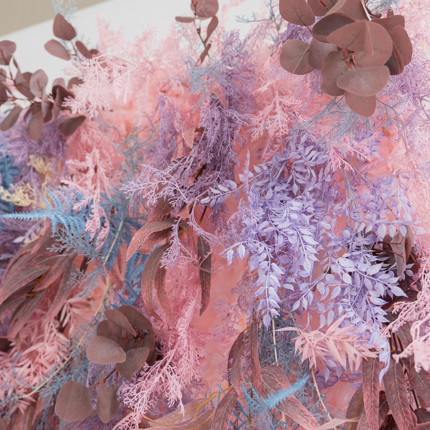This photo showcases a lush, vibrant foliage backdrop. It features a mix of fern - like fronds in shades of blue and purple, along with eucalyptus leaves in earthy brown tones, all blended with soft pink foliage. The harmonious pastel color palette creates a dreamy and romantic atmosphere. Ideal for weddings, parties, or upscale events, it exudes a whimsical and elegant style. 
