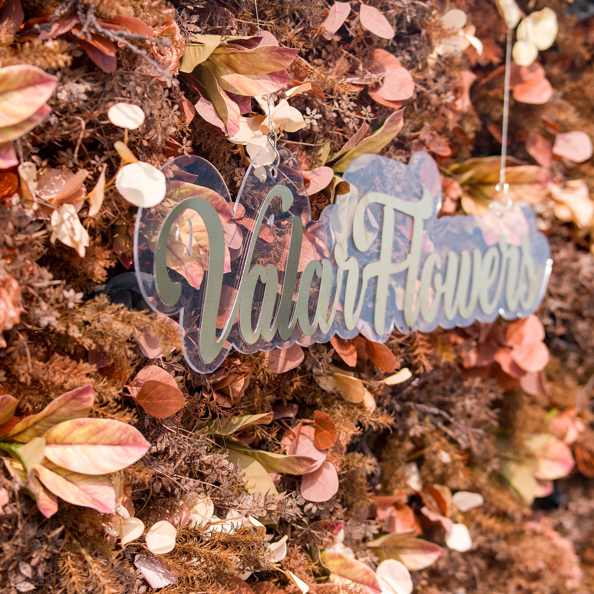 This photo showcases a textured floral backdrop with an array of autumn - colored foliage and muted - toned flowers in shades of rust, brown, and copper. The sign “ValarFlowers” stands out against the rich, earthy hues. Ideal for events like an “Autumn Reverie” wedding or a harvest - themed soirée, it exudes cozy, seasonal charm. 