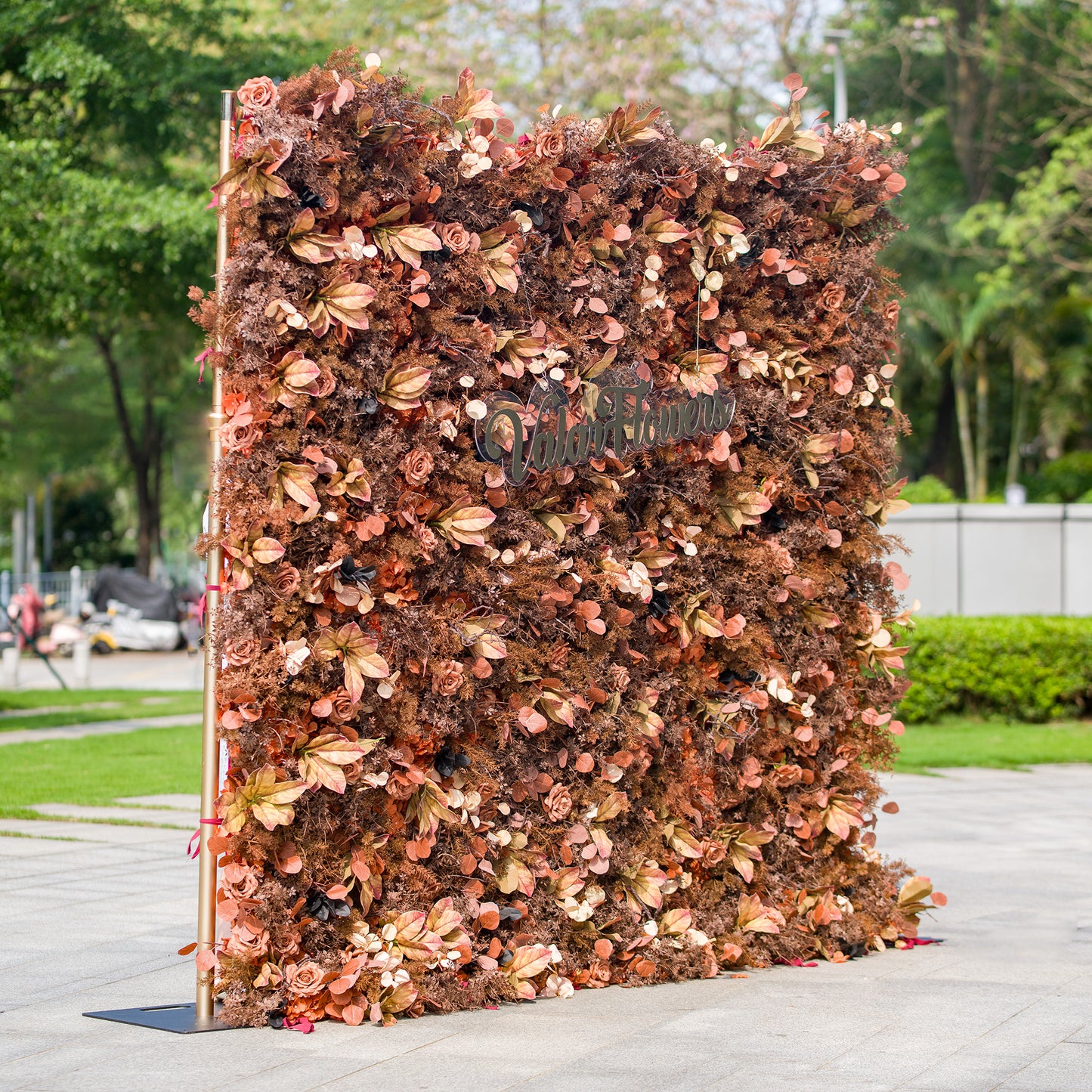 This photo features a large floral backdrop filled with autumn - hued flowers and foliage in shades of rust, brown, and copper. The sign “ValarFlowers” is prominently displayed. Ideal for events like an “Autumn Splendor” wedding or a fall - themed corporate event, it exudes warm, rustic charm, perfect for seasonal celebrations. 