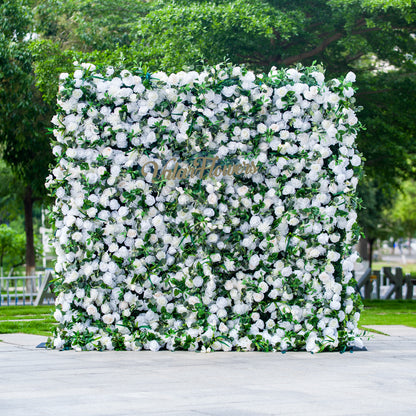 This photo showcases a large, square floral backdrop densely covered with white flowers, likely roses, interspersed with lush green foliage. The text “ValarFlowers” in elegant golden lettering stands out prominently. Ideal for events like a “Pure Elegance” wedding or a formal garden party, it exudes a sophisticated and serene atmosphere, perfect for upscale outdoor celebrations. 