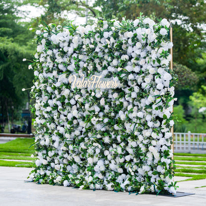 This photo showcases a large, square floral backdrop densely adorned with white flowers, likely roses and hydrangeas, interspersed with lush green foliage. The text “ValarFlowers” in elegant golden lettering stands out prominently. Ideal for events like a “White Elegance” wedding or a formal garden reception, it exudes a sense of purity and sophistication, perfect for upscale outdoor celebrations. 