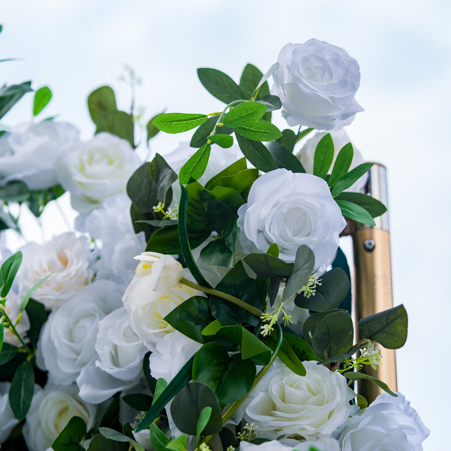 This photo showcases a lush arrangement of white roses, interspersed with green foliage. The blooms are in full display, creating a pure and elegant look. Ideal for events like a “Winter Wonderland” themed wedding or a sophisticated anniversary celebration, it exudes a sense of timeless beauty and refinement, perfect for upscale indoor or outdoor gatherings. 