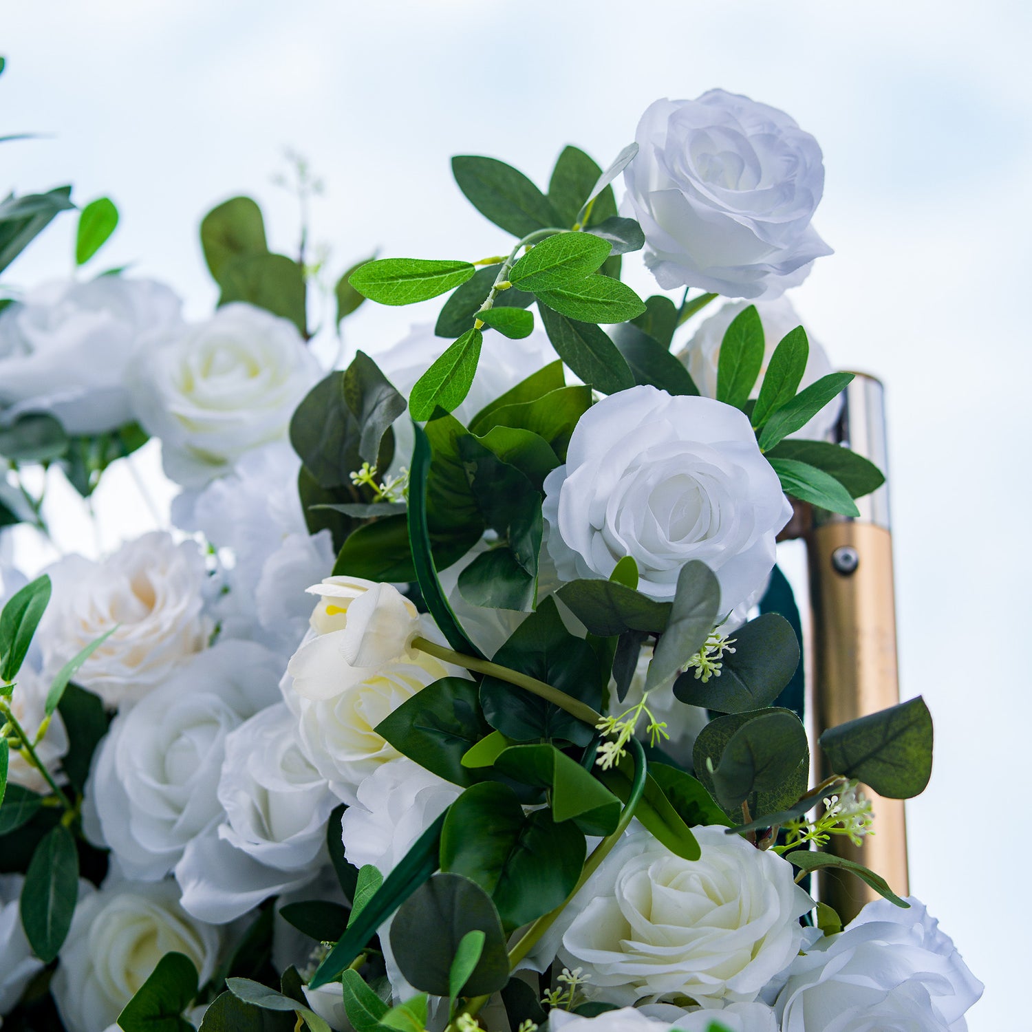 This photo showcases a lush arrangement of white roses, interspersed with green foliage. The blooms are in full display, creating a pure and elegant look. Ideal for events like a “Winter Wonderland” themed wedding or a sophisticated anniversary celebration, it exudes a sense of timeless beauty and refinement, perfect for upscale indoor or outdoor gatherings. 