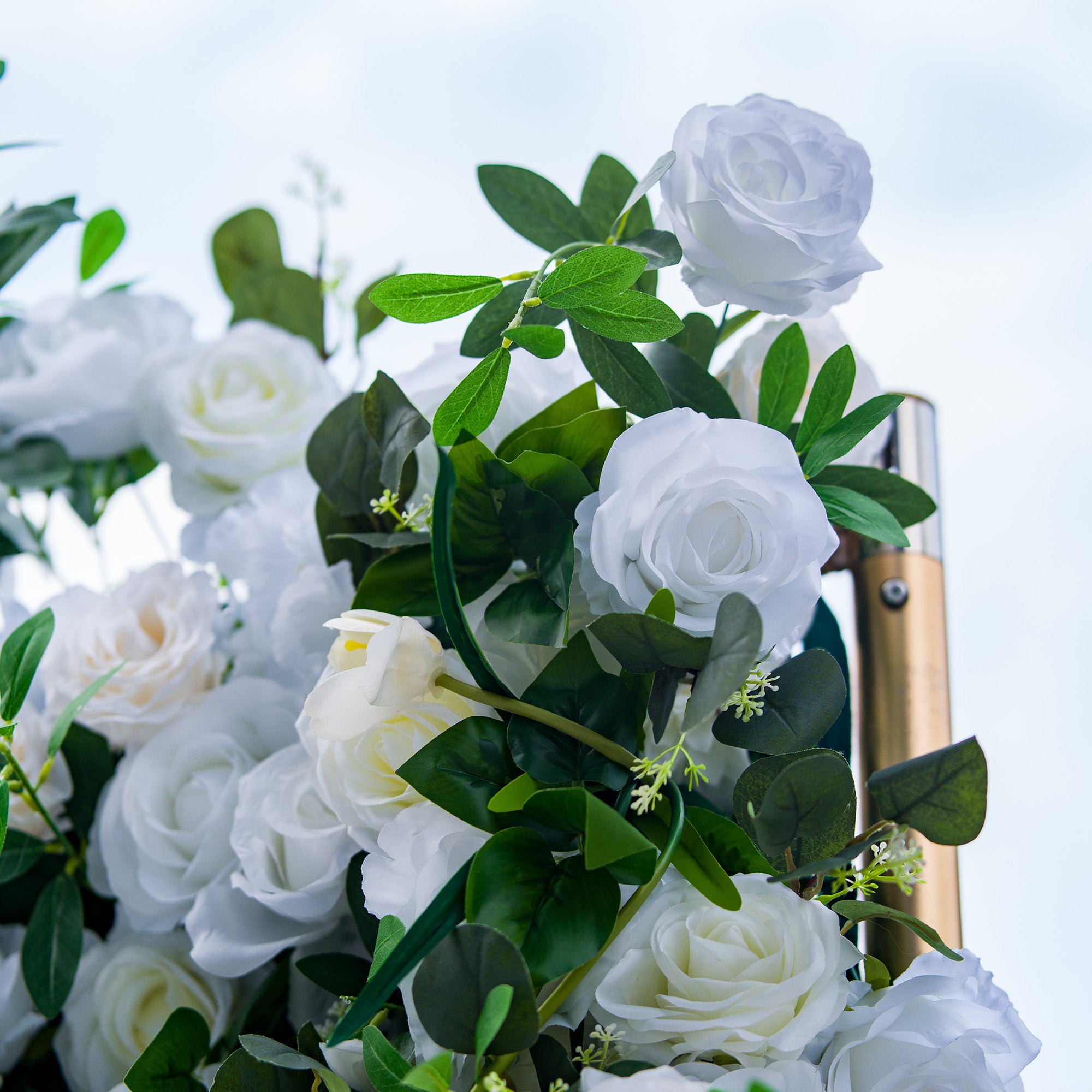 This photo showcases a lush arrangement of white roses, interspersed with green foliage. The blooms are in full display, creating a pure and elegant look. Ideal for events like a “Winter Wonderland” themed wedding or a sophisticated anniversary celebration, it exudes a sense of timeless beauty and refinement, perfect for upscale indoor or outdoor gatherings. 
