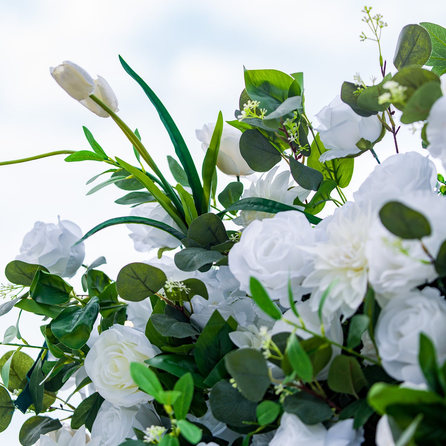 This photo showcases a lush arrangement of white roses, tulips, and other white blooms, set against rich green foliage. The flowers create a serene and elegant display. Ideal for events like a “Pure Bliss” wedding or a refined garden reception, it exudes a sense of purity and sophistication, perfect for upscale and graceful gatherings. 