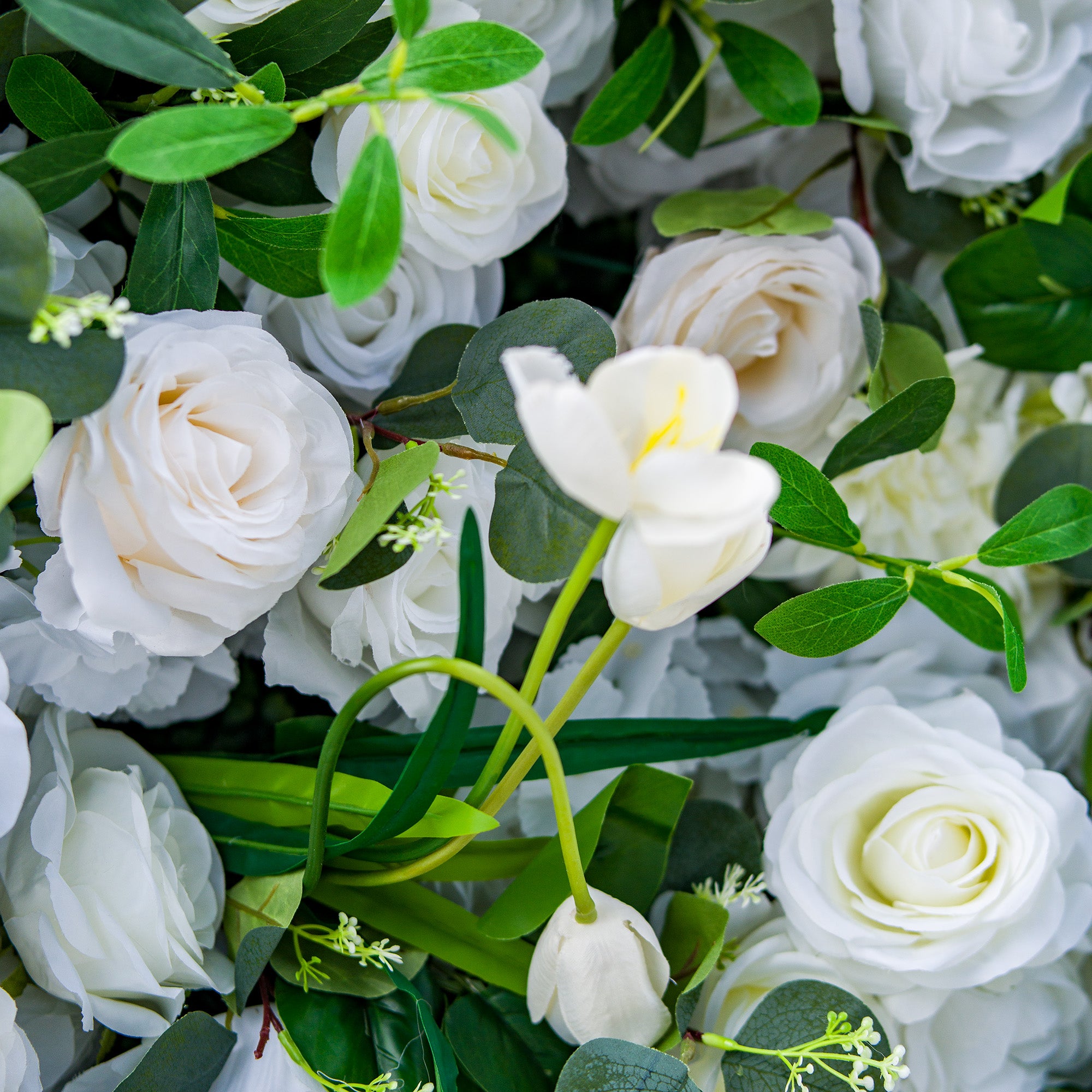 This photo showcases a lush arrangement of white roses and tulips, interspersed with green foliage. The delicate white blooms create an elegant and serene display. Ideal for events like a “Heavenly White” wedding or a sophisticated garden party, it exudes a sense of purity and refinement, perfect for upscale and graceful celebrations. 