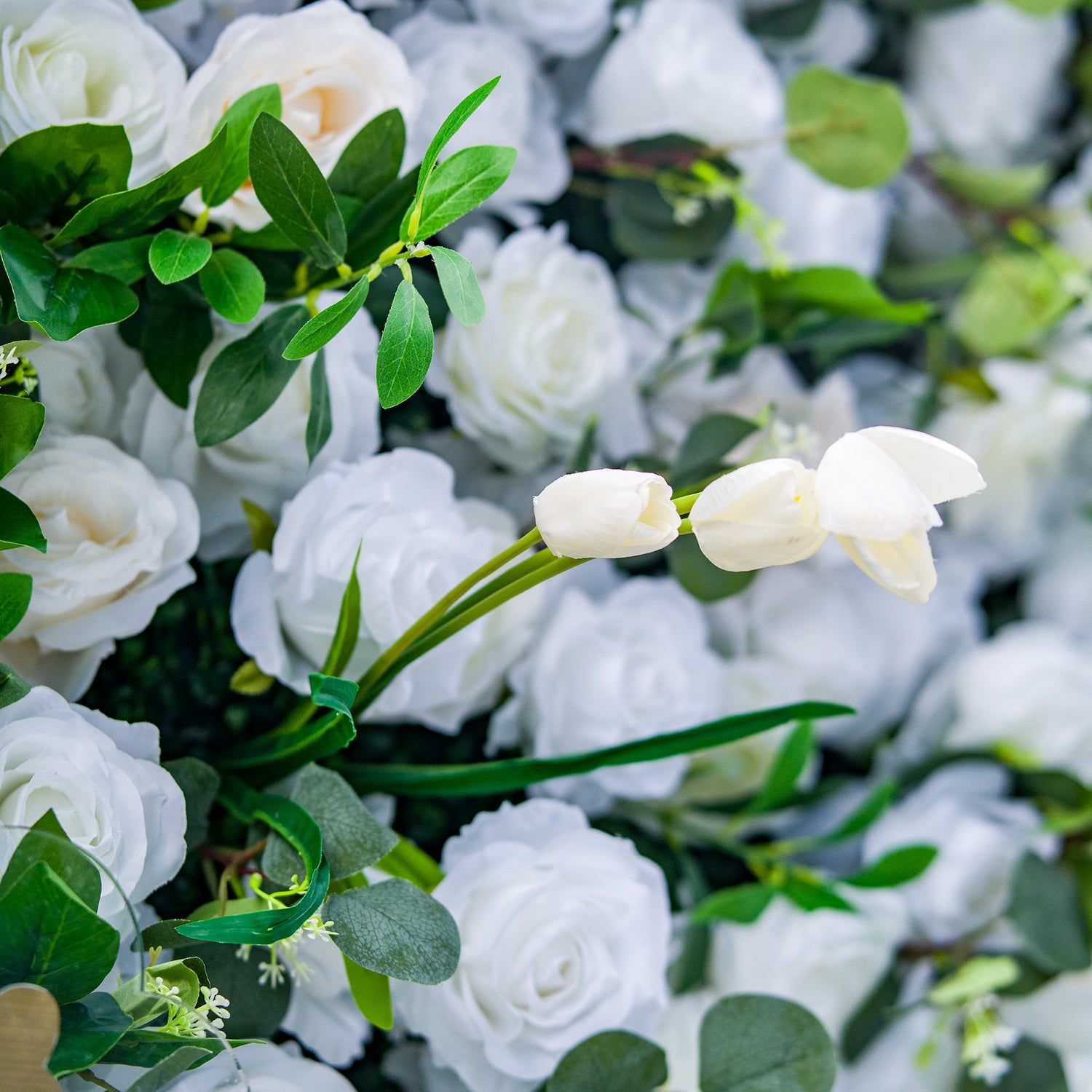 This photo features a lush arrangement of white roses and tulips, set against a backdrop of green foliage. The delicate white blooms create an elegant and serene display. Ideal for events like a “White Elegance” wedding or a refined garden party, it exudes a sense of purity and sophistication, perfect for upscale and graceful celebrations. 