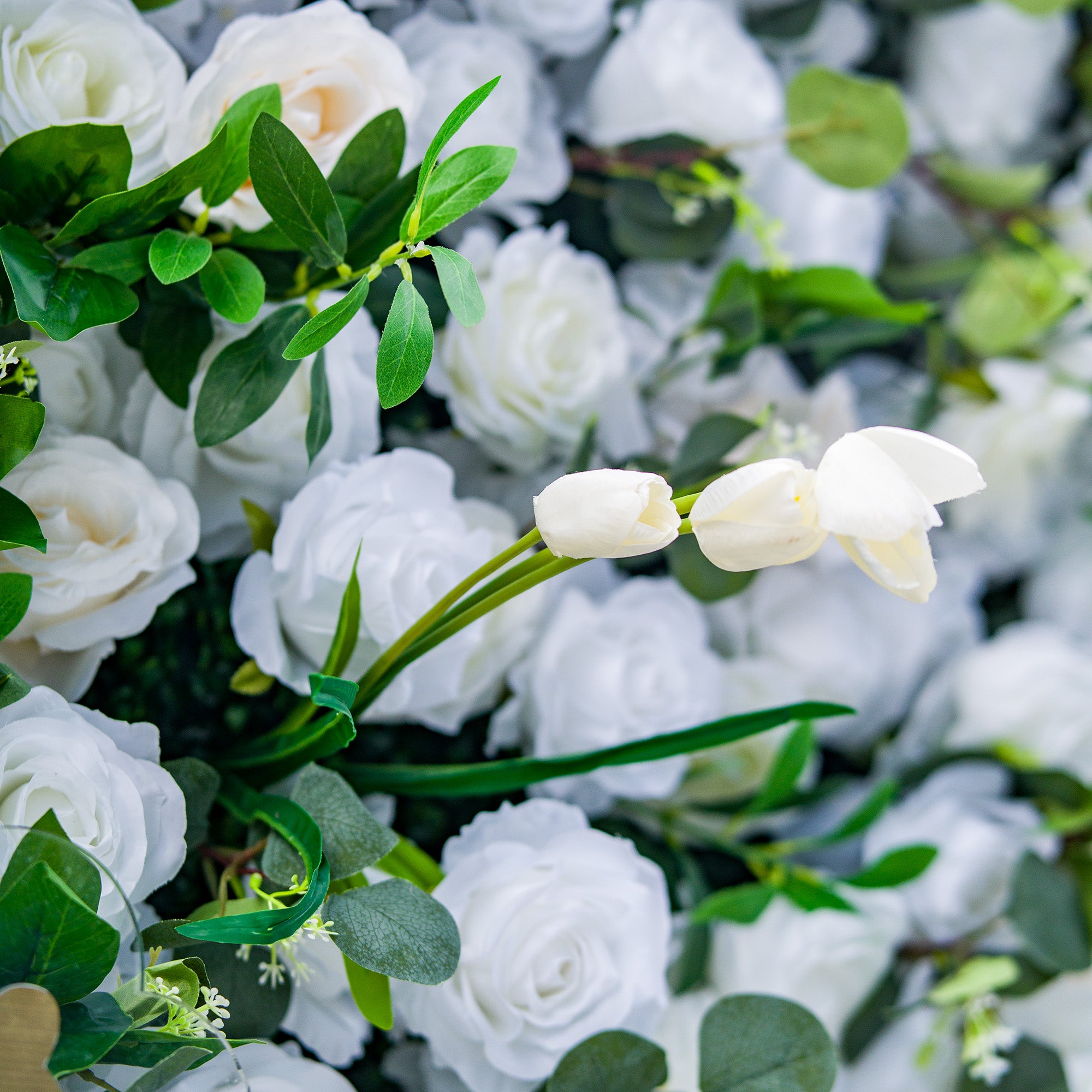 This photo features a lush arrangement of white roses and tulips, set against a backdrop of green foliage. The delicate white blooms create an elegant and serene display. Ideal for events like a “White Elegance” wedding or a refined garden party, it exudes a sense of purity and sophistication, perfect for upscale and graceful celebrations. 
