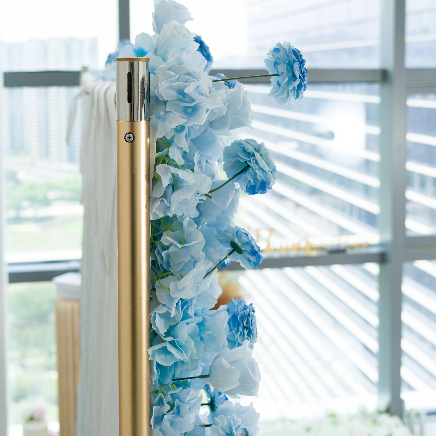 This photo features a gold pole adorned with blue hydrangeas and delicate blue flowers. The monochromatic light - blue color theme creates a serene, elegant vibe, perfect for events like weddings, baby showers, or upscale gatherings. The modern backdrop of glass windows and an urban skyline adds a sophisticated touch. The cohesive hue and realistic faux flowers offer a polished, long - lasting decorative element, ideal for setting a tranquil and refined mood at any celebration. 