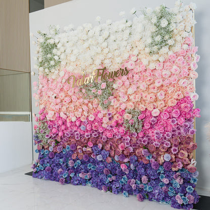 This stunning floral wall by ValarFlowers features a gradient of blooms—white roses and baby’s breath at the top, transitioning to soft pink, lavender, and deep purple flowers. The gold “ValarFlowers” logo adds elegance. Set indoors against a minimalist backdrop, it’s perfect for weddings, events, or photo backdrops, blending romance and sophistication. 