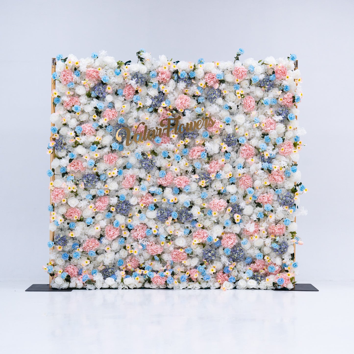 This photo features a stunning floral backdrop from Valar Flowers, showcasing a dense arrangement of artificial flowers in various shades of pink, blue, and white. The gold lettering of "ValarFlowers" adds a touch of elegance, making it an ideal decorative piece for weddings, photo shoots, or other special events. The meticulous arrangement of the flowers enhances the overall aesthetic, adding a touch of natural beauty and charm to any setting.
