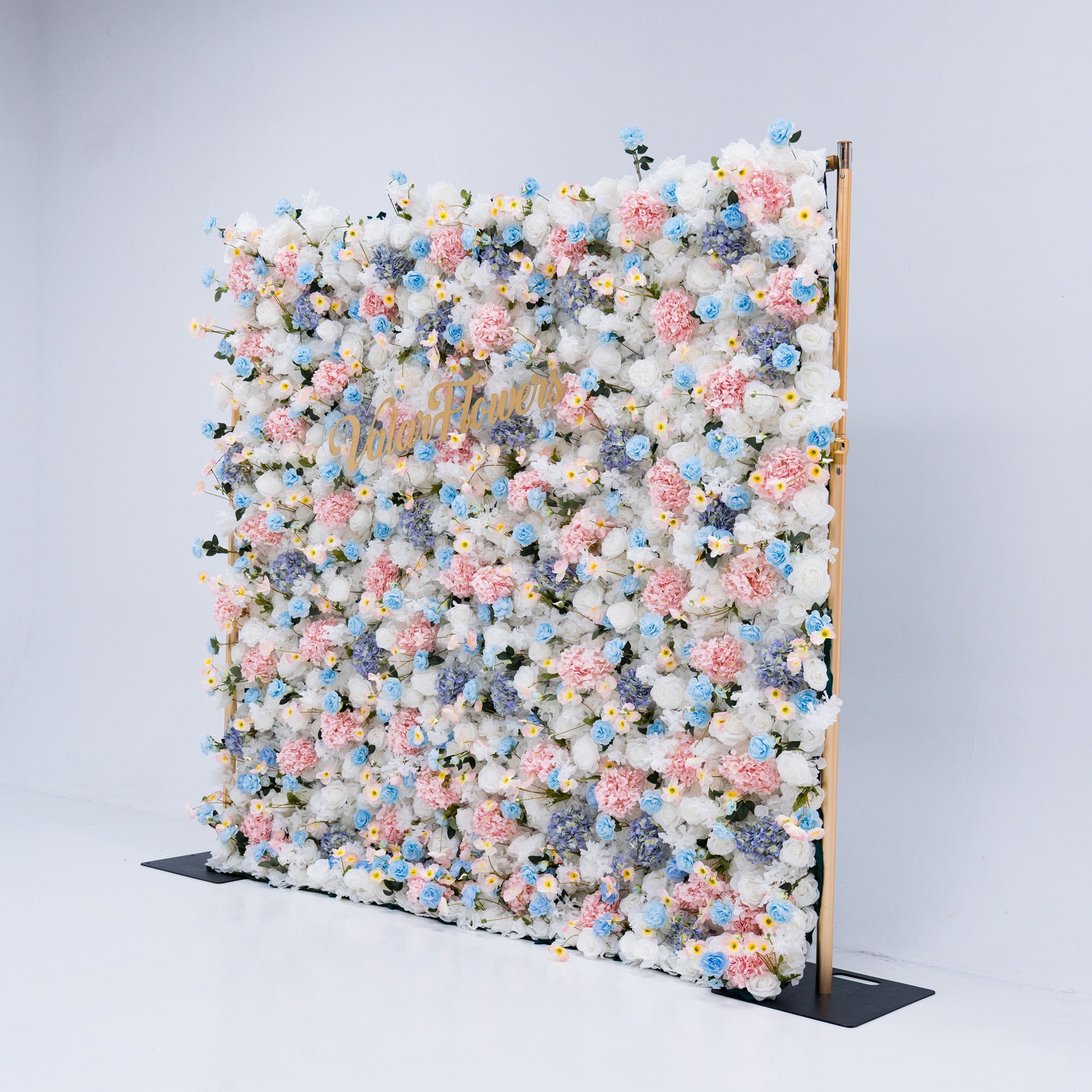This photo showcases a magnificent floral backdrop from Valar Flowers, featuring a dense arrangement of artificial flowers in various shades of pink, blue, and white. The gold lettering of "ValarFlowers" adds a touch of elegance and sophistication, making it an ideal decorative piece for weddings, photo shoots, or other special events. The meticulous arrangement of the flowers enhances the overall aesthetic, adding a touch of natural beauty and charm to any setting.