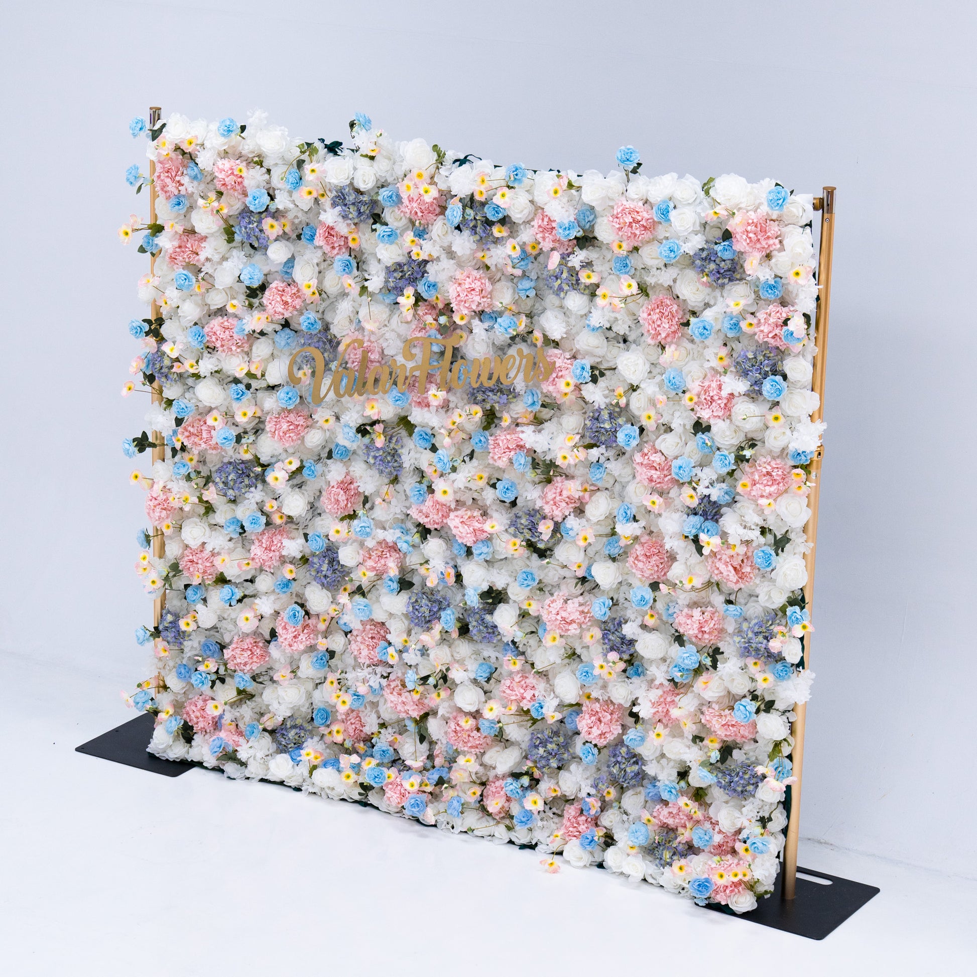 This photo showcases a magnificent floral backdrop from Valar Flowers, featuring a dense arrangement of artificial flowers in various shades of pink, blue, and white. The gold lettering of "Valar Flowers" adds a touch of elegance and sophistication, making it an ideal decorative piece for weddings, photo shoots, or other special events. The meticulous arrangement of the flowers enhances the overall aesthetic, adding a touch of natural beauty and charm to any setting.