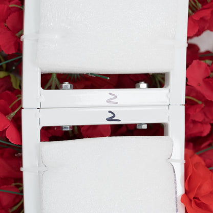 Close - up of two stacked white metal frames, each labeled “2” and padded with foam. Surrounding them are red artificial flowers. The frames, with visible bolts, seem to be parts of a decorative floral structure, likely for assembly into a larger decorative piece. 