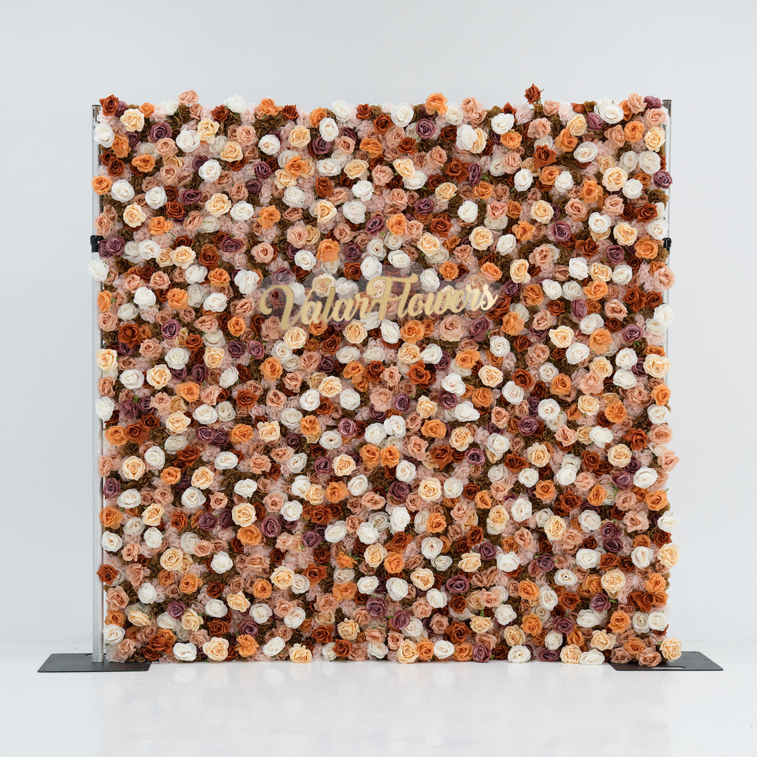 A large floral backdrop features an array of artificial flowers in shades of beige, white, and brown. At its center, “ValarFlowers” is written in gold script. The dense, varied blooms create a textured, elegant display, perfect for events or photo opportunities. 