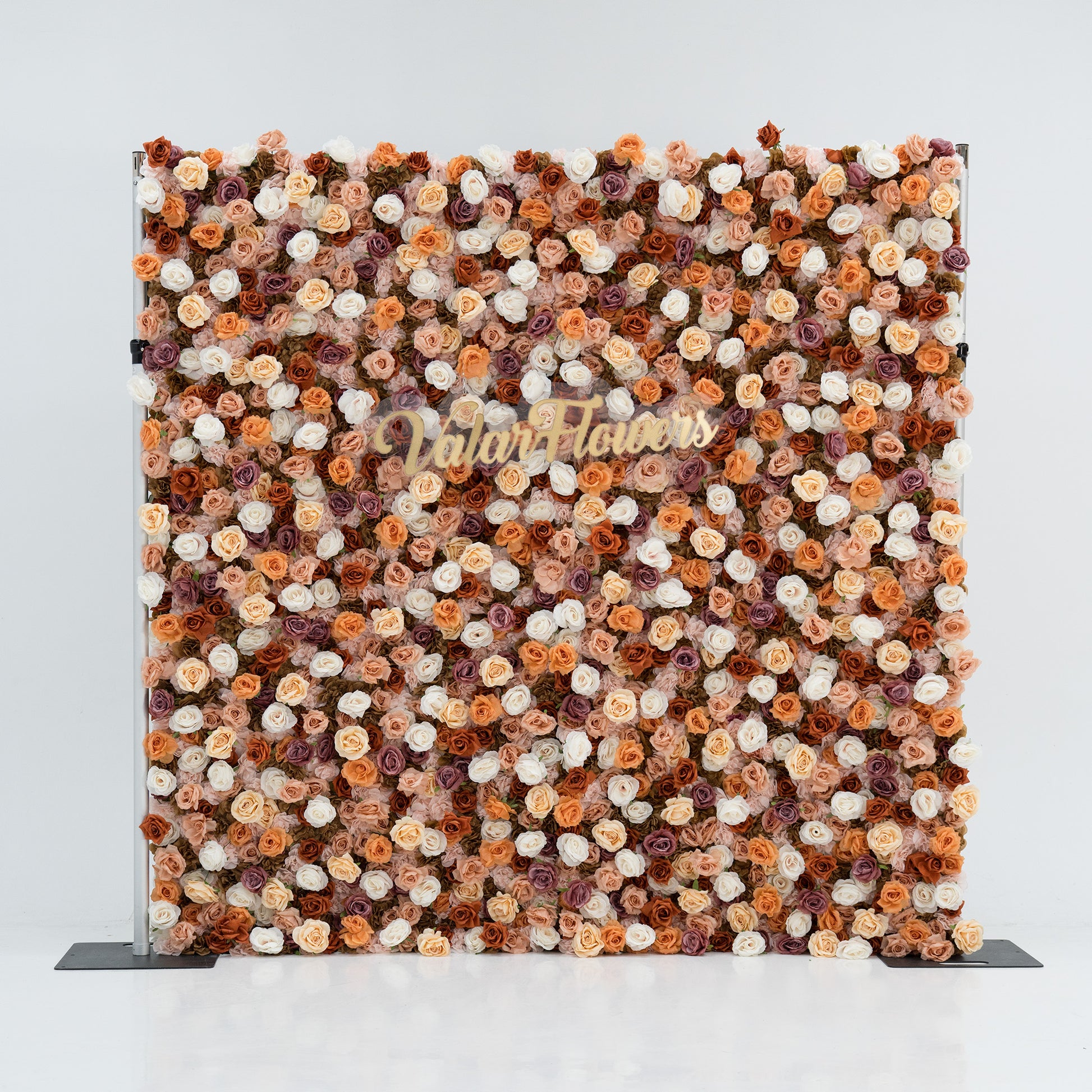 A large floral backdrop features an array of artificial flowers in shades of beige, white, and brown. At its center, “ValarFlowers” is written in gold script. The dense, varied blooms create a textured, elegant display, perfect for events or photo opportunities. 