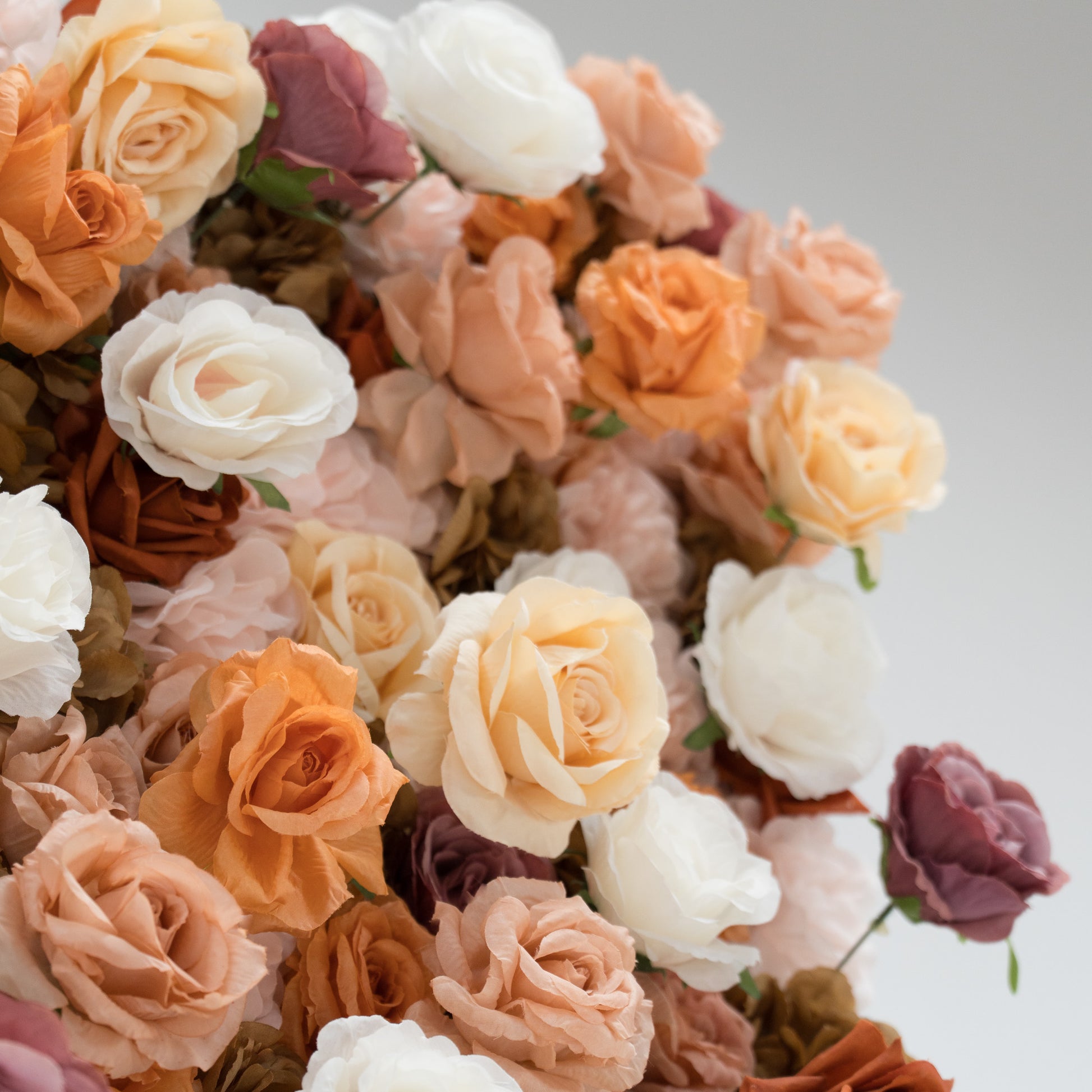 A large artificial flower wall features a mix of beige, white, and purple blooms. In the center, “ValarFlowers” is displayed in gold script. The wall is supported by metal poles and bases, creating an elegant, textured backdrop ideal for events or decor. 
