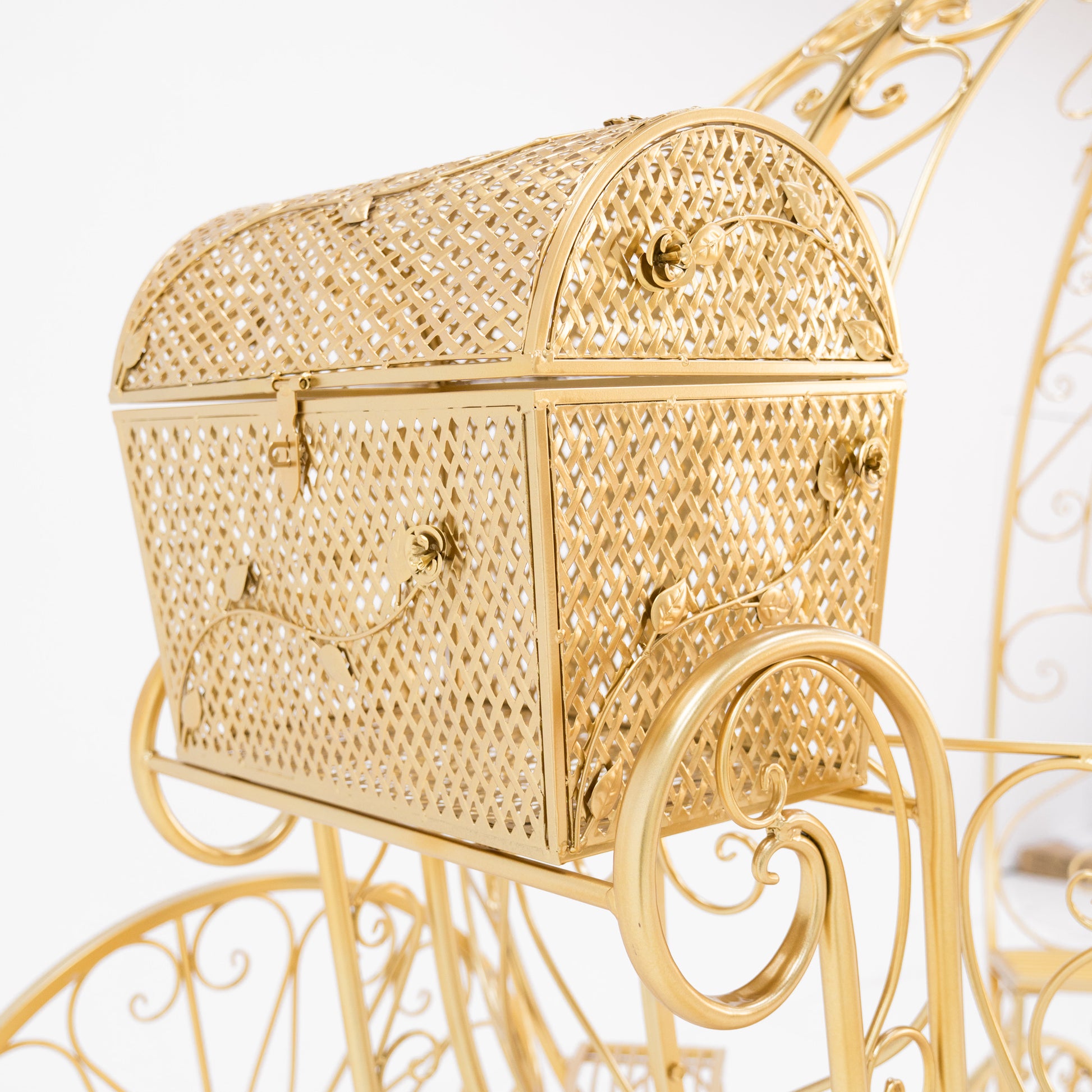 A close - up of a gold - toned, ornate metal trunk. Part of a Disney - style Cinderella carriage, it features intricate latticework, decorative floral motifs, and small clasps. The shimmering gold finish and detailed design add a fairy - tale charm, perfect for themed displays. 