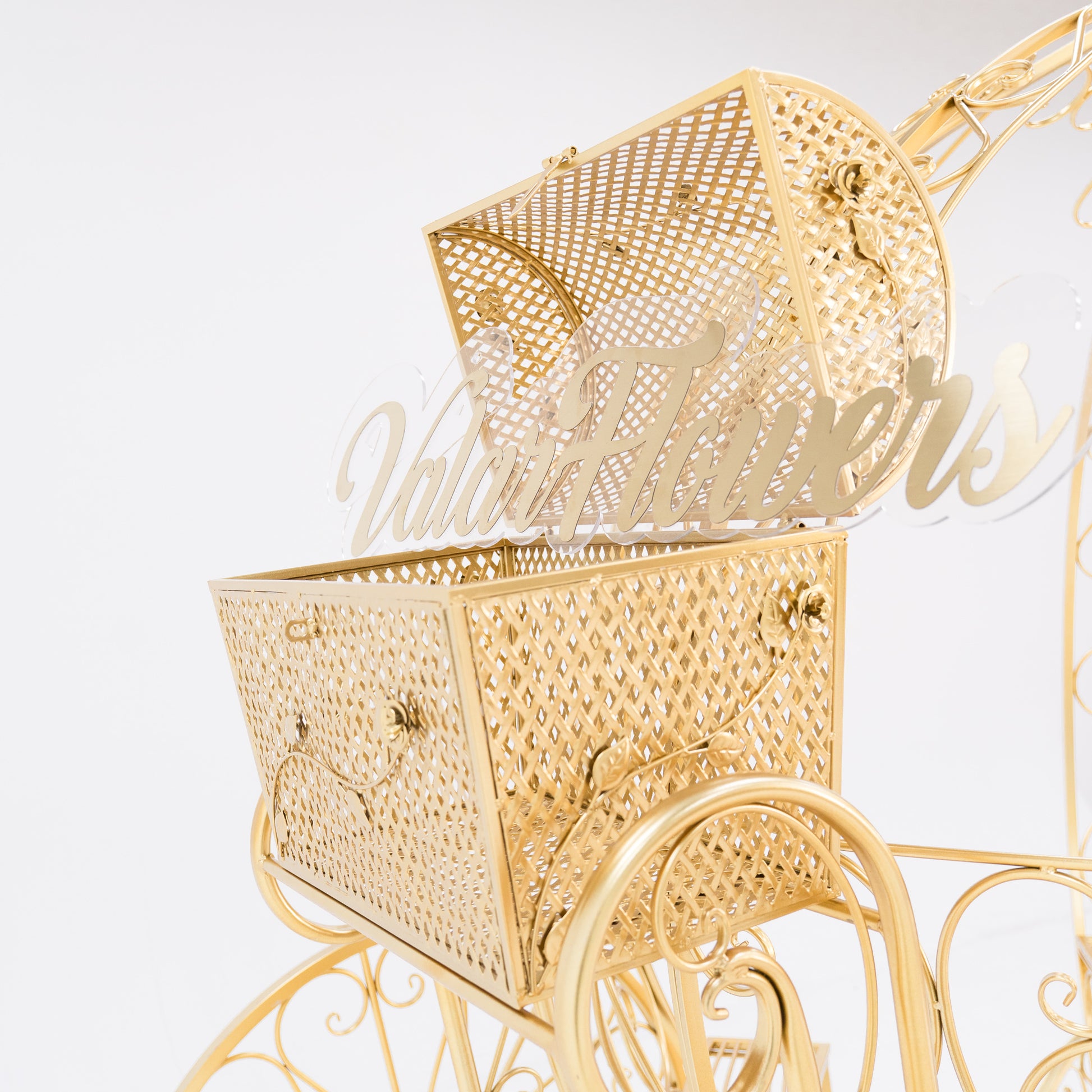 A close - up of a gold, ornate metal trunk with latticework, part of a Cinderella - style carriage. The lid is open, revealing a clear acrylic “ValarFlowers” sign inside. Decorative floral motifs and clasps enhance its fairy - tale charm, perfect for themed displays. 