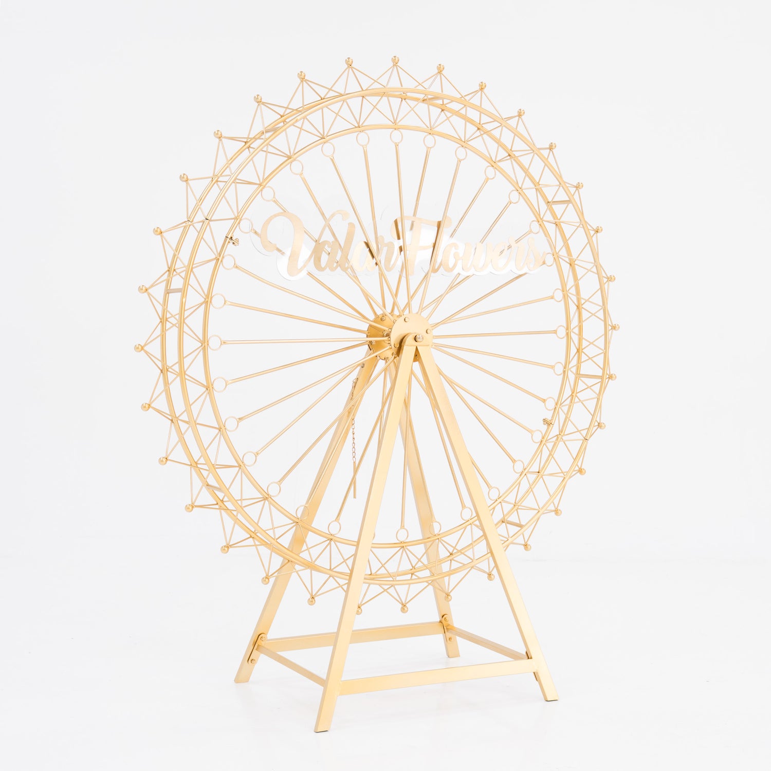 A golden, metal Ferris wheel decoration with a triangular stand. It features intricate spokes and small spheres along the rim. In the center, a stylish, cursive “ValarFlowers” sign adds branding. Ideal for decorative, themed event setups. 