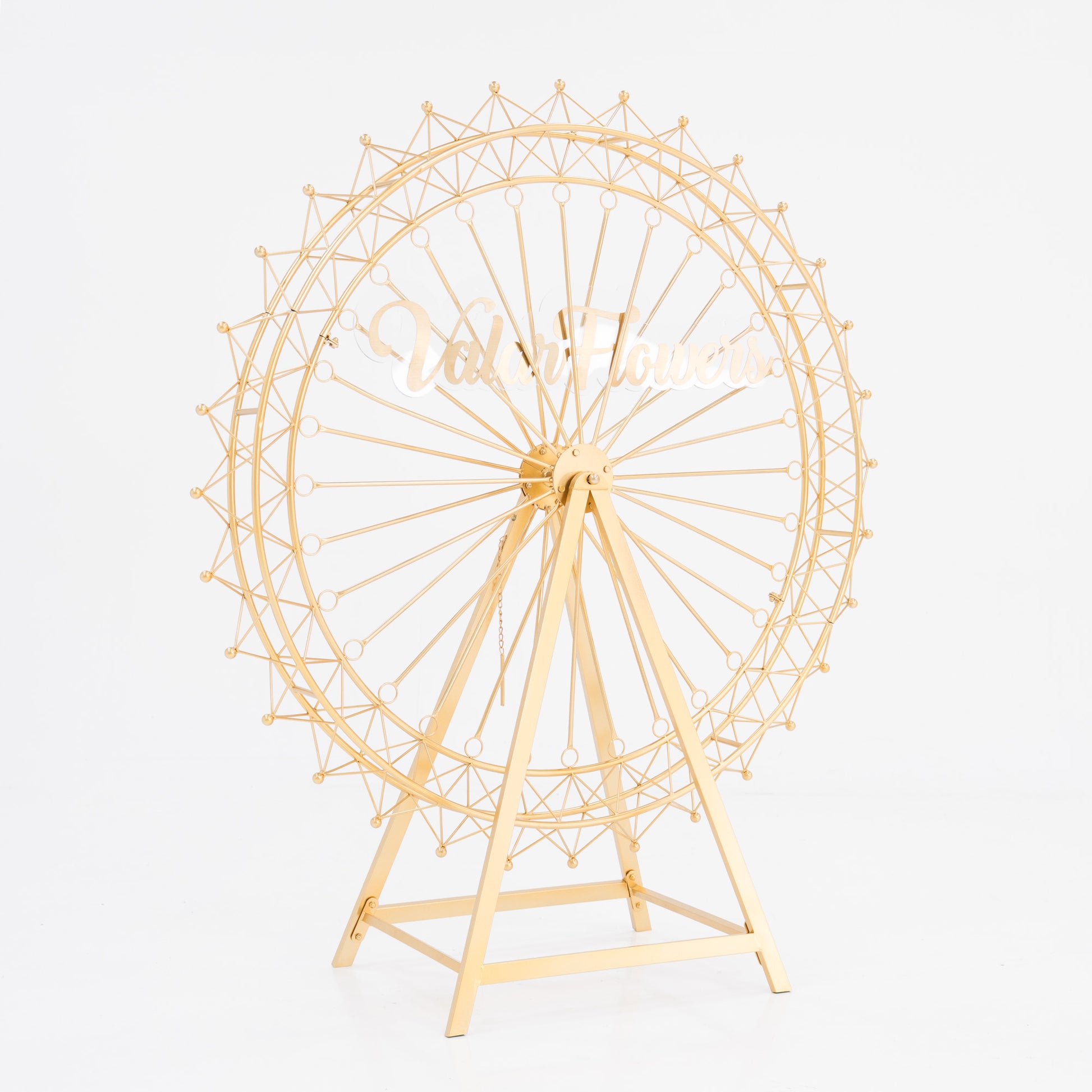A golden, metal Ferris wheel decoration with a triangular stand. It features intricate spokes and small spheres along the rim. In the center, a stylish, cursive “ValarFlowers” sign adds branding. Ideal for decorative, themed event setups. 