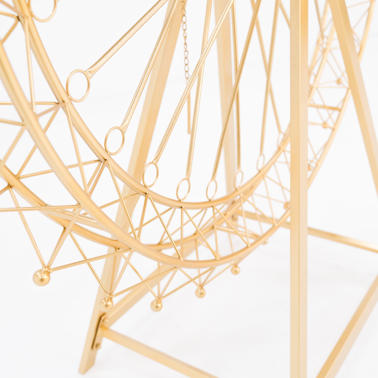 Close - up of a golden Ferris wheel decoration's lower half. Features intricate, geometric metalwork with circular loops and small spheres. The triangular stand and chain add detail, showcasing elegant, decorative craftsmanship. 