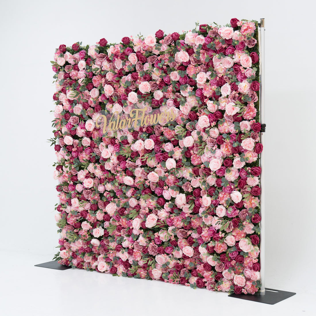A large artificial flower wall, densely packed with pink and deep - pink roses, plus green foliage. A gold “ValarFlowers” sign is centered, creating an elegant, romantic backdrop—ideal for events, exuding charm and sophistication. 