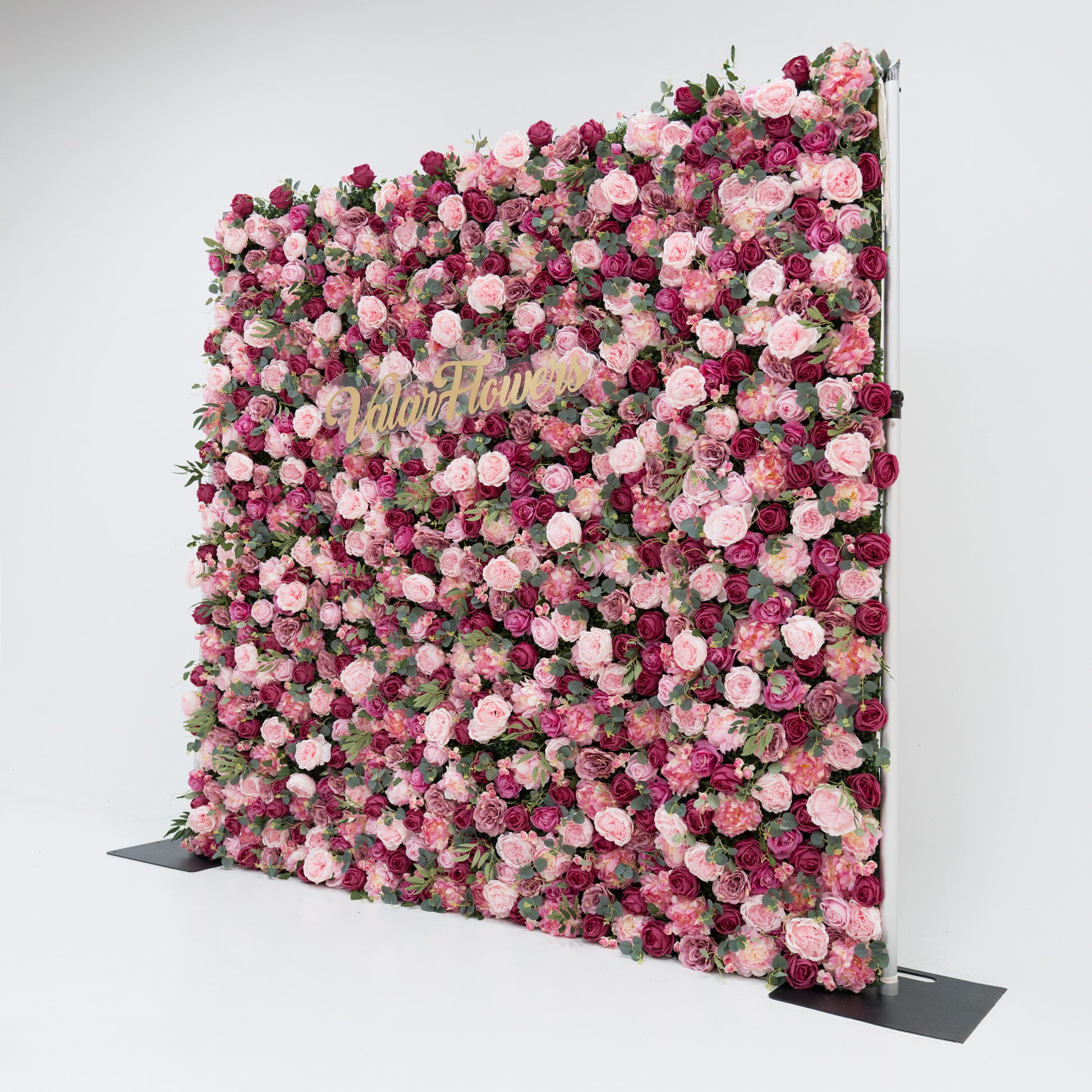 A large artificial flower wall, a vibrant mix of pink, deep - pink roses, and green foliage. A gold “ValarFlowers” sign is centrally placed, creating a romantic, elegant backdrop—ideal for events, exuding charm and sophistication with its lush, colorful blooms. 
