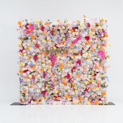 A large, square floral wall bursts with a vibrant mix of colorful artificial flowers—pink, yellow, orange, purple, and more. Dense clusters create a lush, lively display. With the “Valor Flowers” sign in the center, set against a plain white background and floor, it exudes a cheerful, festive vibe, perfect for events like weddings, parties, or as a decorative photo backdrop.