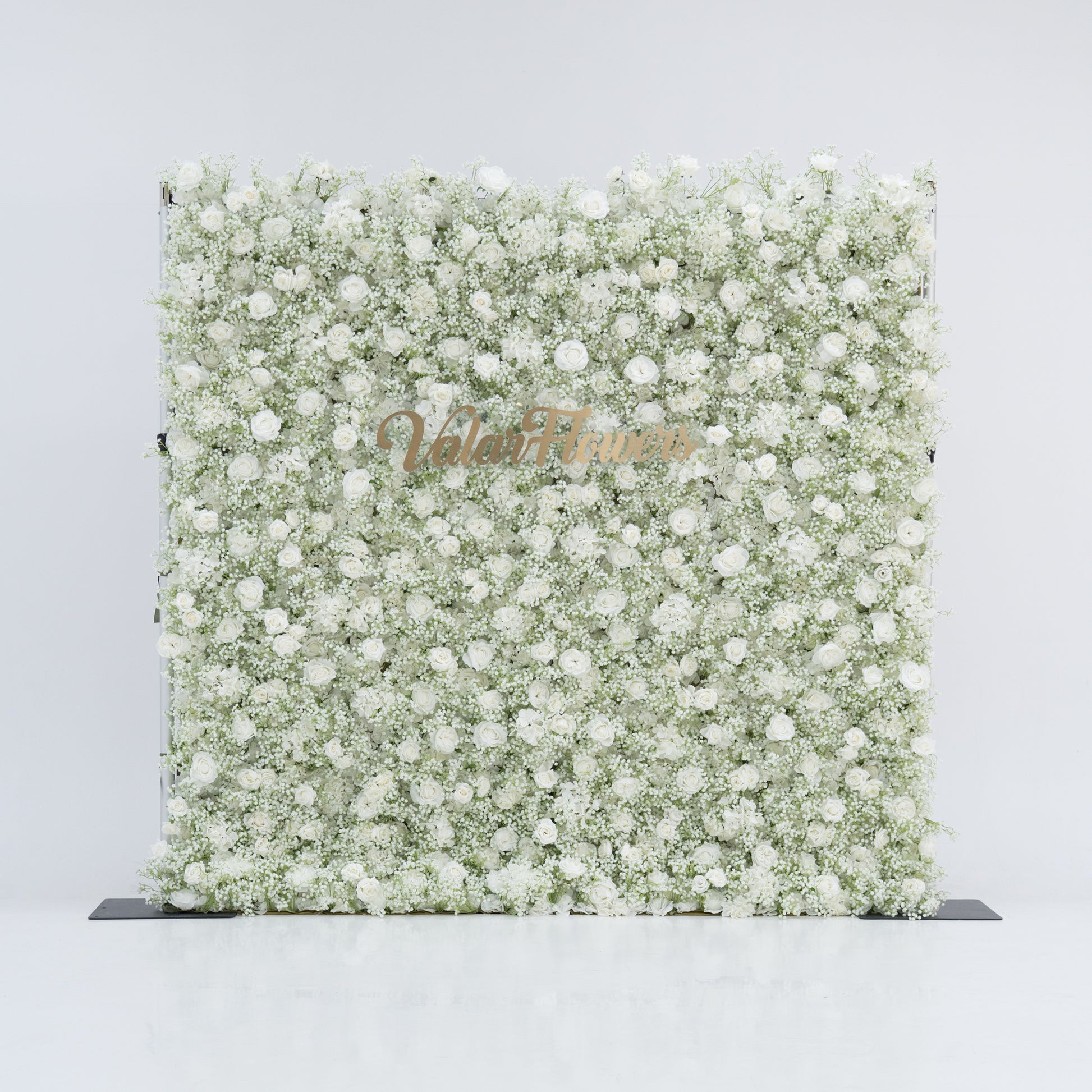 This image showcases a large, square floral wall densely covered with white flowers, including baby's breath and small blooms. "Valar Flowers" is displayed in elegant golden text. Set against a plain white background, the wall exudes a pure, elegant, and refined atmosphere, perfect for decorative purposes in events or as a stylish backdrop, highlighting the beauty of natural flowers.