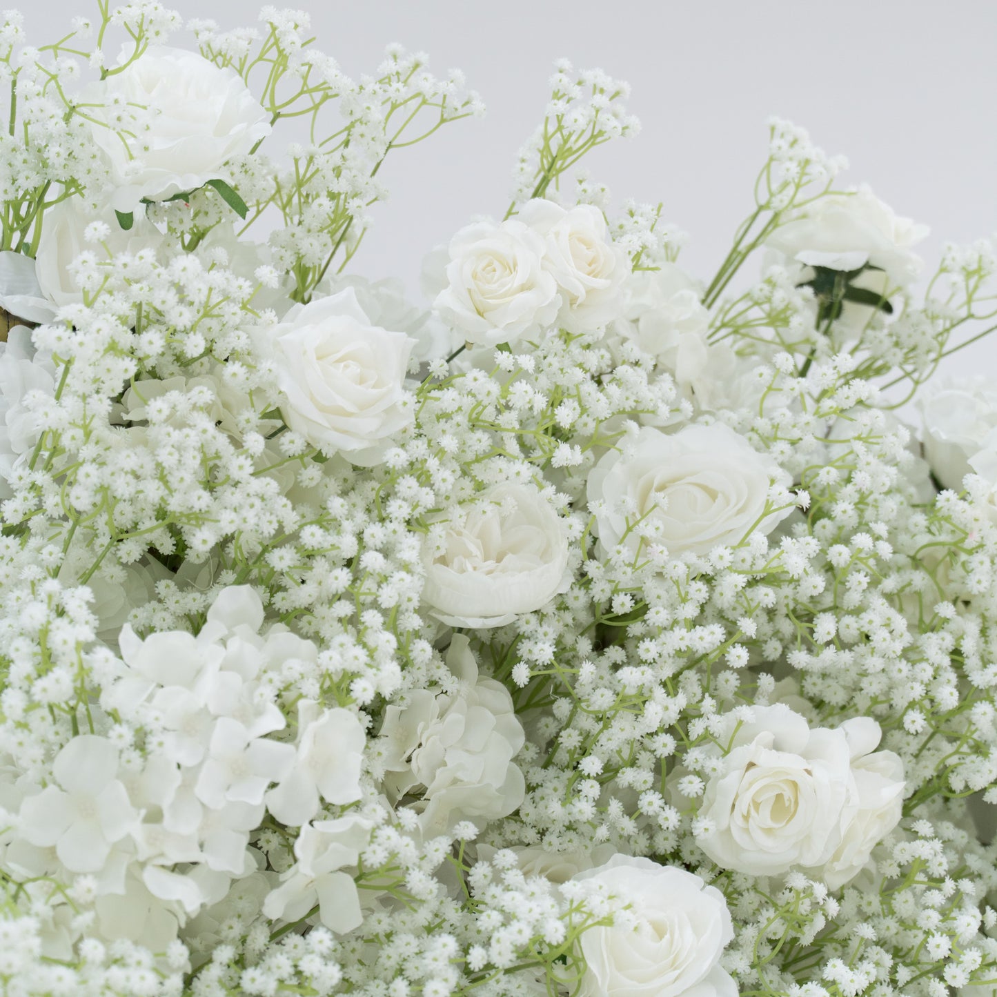 This image presents a lush arrangement of white flowers, including roses, hydrangeas, and baby's breath. The blooms are densely clustered, creating a soft, elegant, and pure visual effect. Set against a plain white background, the flowers exude a sense of tranquility and beauty, perfect for decorative purposes in events or as a symbol of innocence and grace.