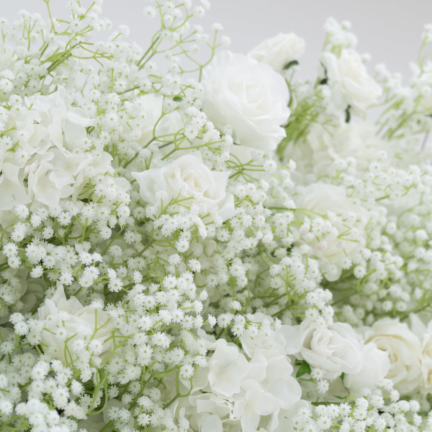 This image presents a lush arrangement of white flowers, including roses, hydrangeas, and baby's breath. The blooms are densely clustered, creating a soft, elegant, and pure visual effect. Set against a plain white background, the flowers exude a sense of tranquility and beauty, perfect for decorative purposes in events or as a symbol of innocence and grace.